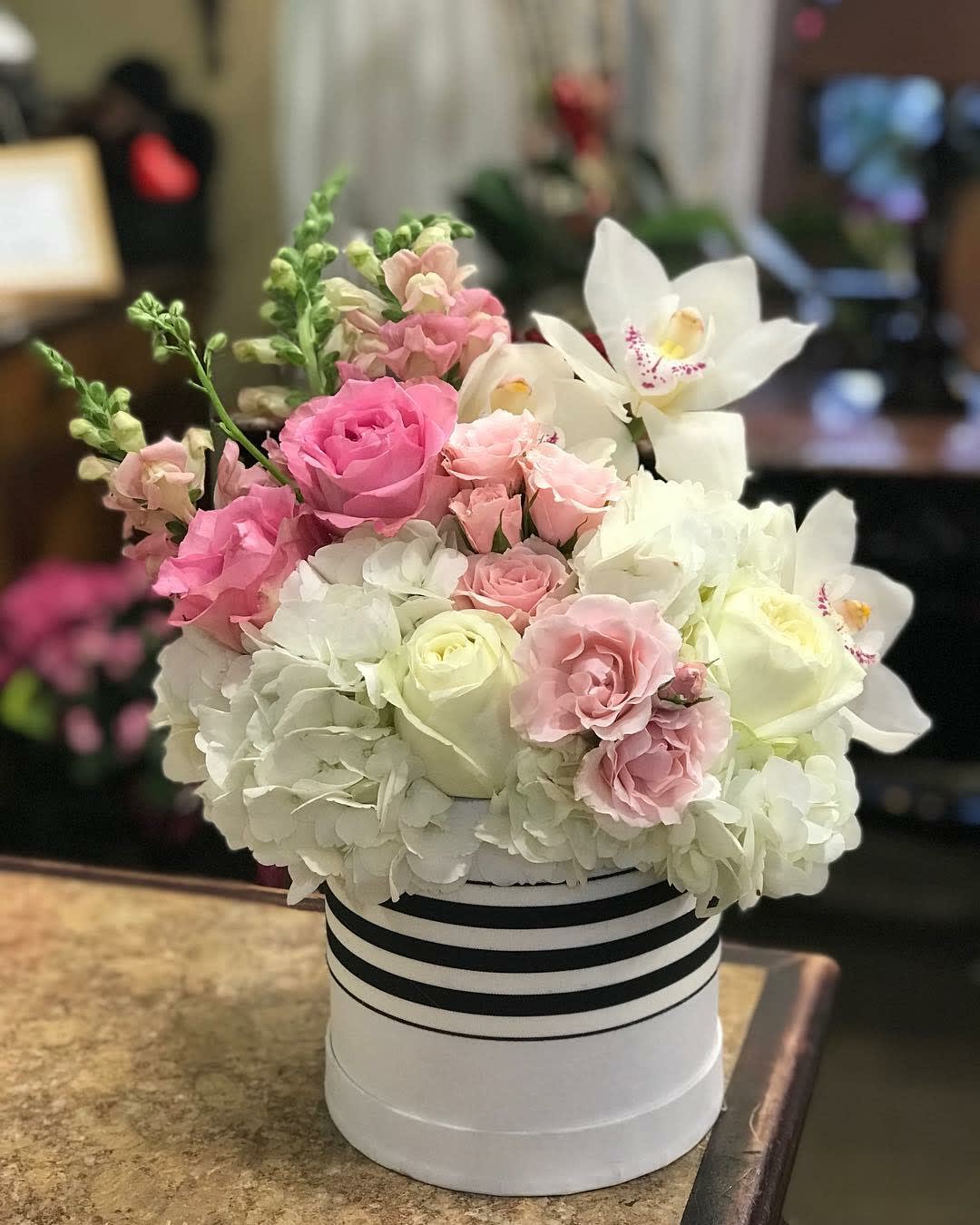 Pink and white roses with white orchids in a striped hat box