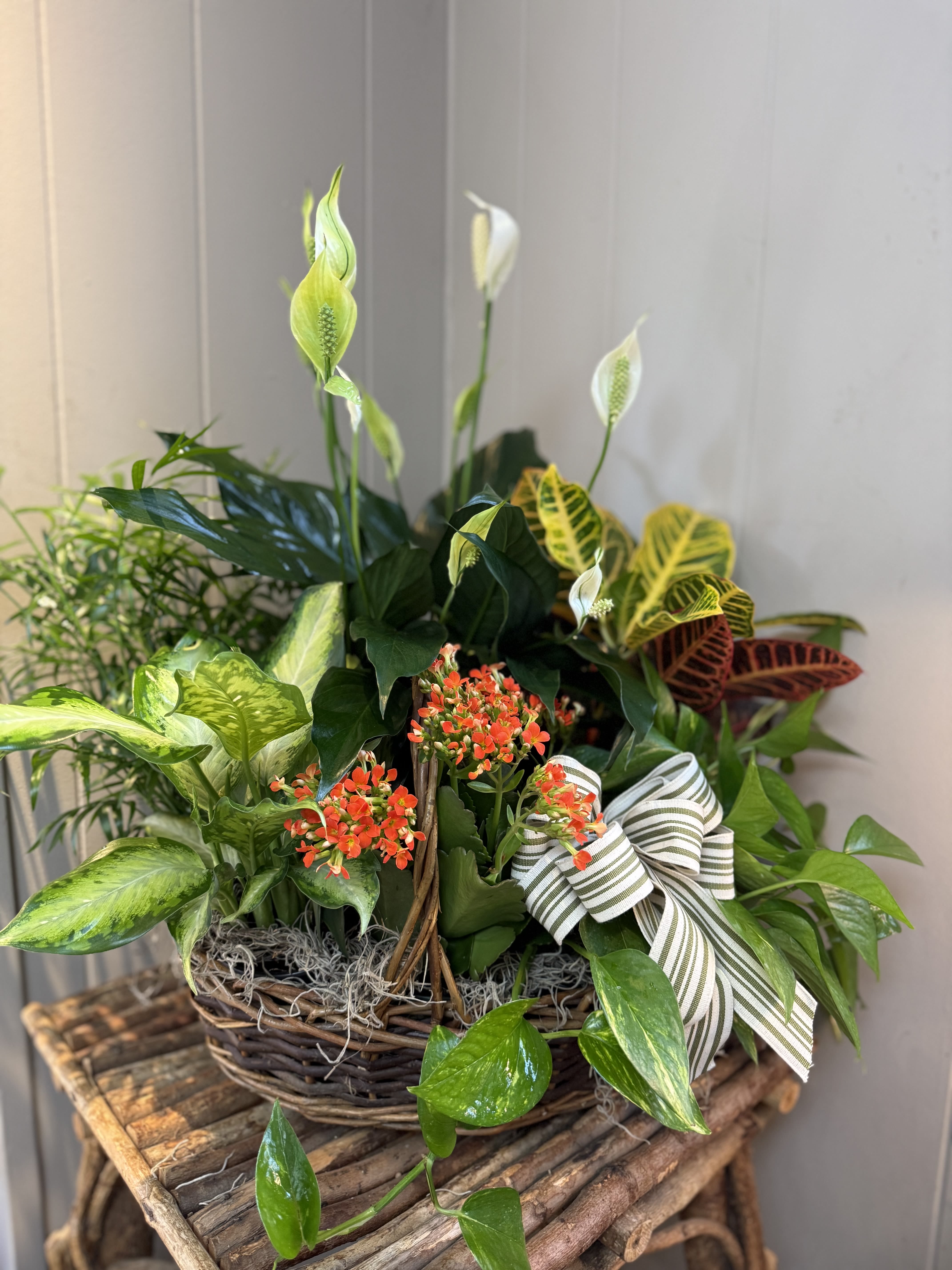 Basket planter with white peace lilies, orange blooms, and assorted foliage