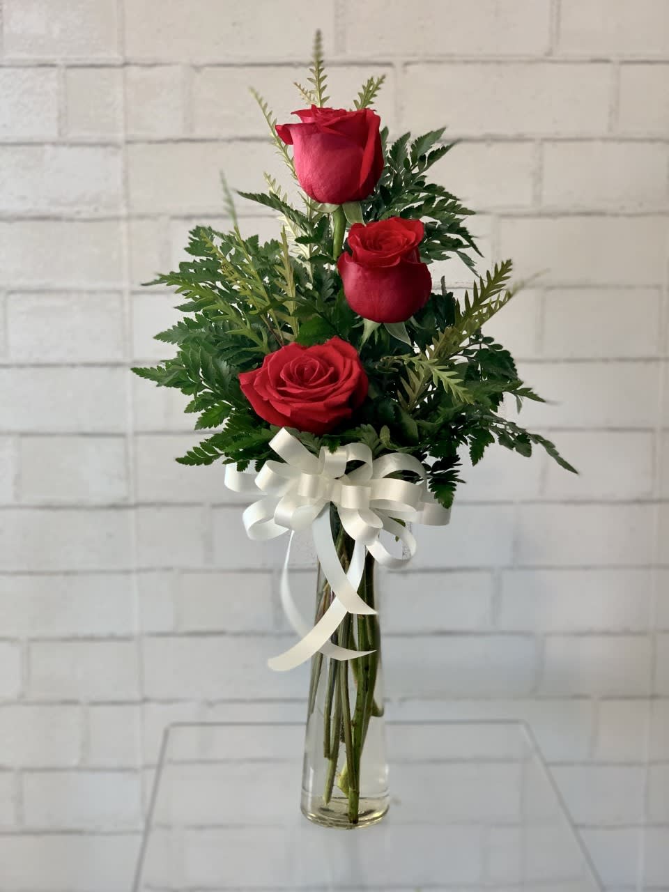 Three red roses in a clear glass vase with a white ribbon