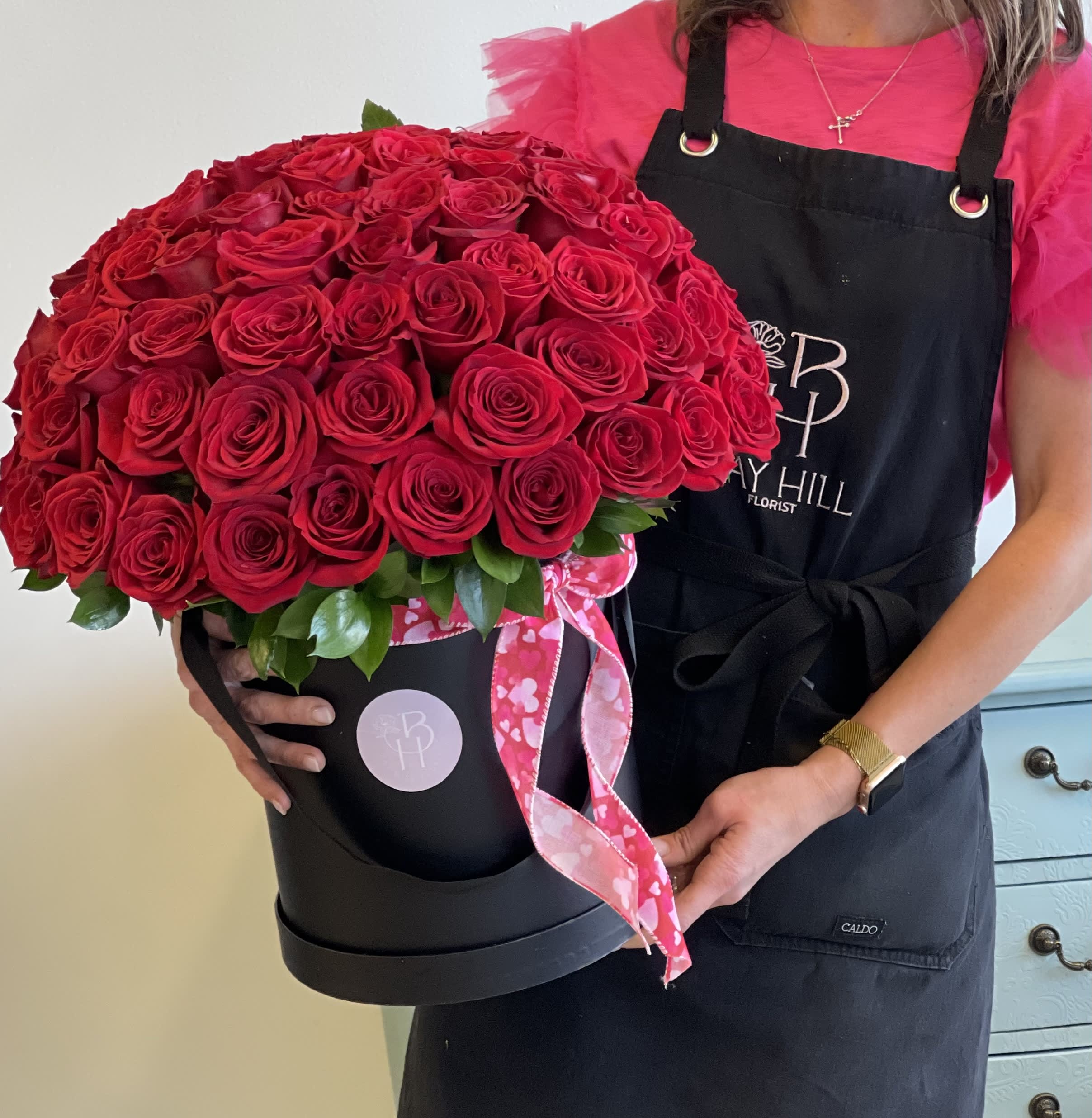 Large red rose arrangement in a black hatbox with a pink ribbon