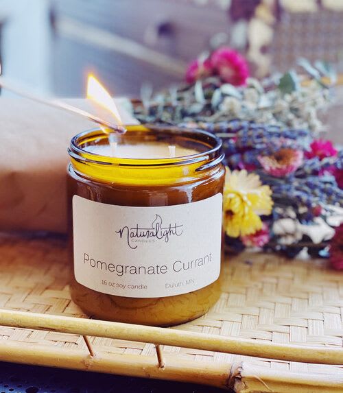 Amber glass jar pomegranate currant candle being lit on a woven tray with dried flowers behind