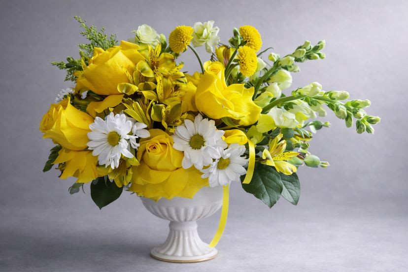 Yellow and white floral arrangement in a white pedestal vase