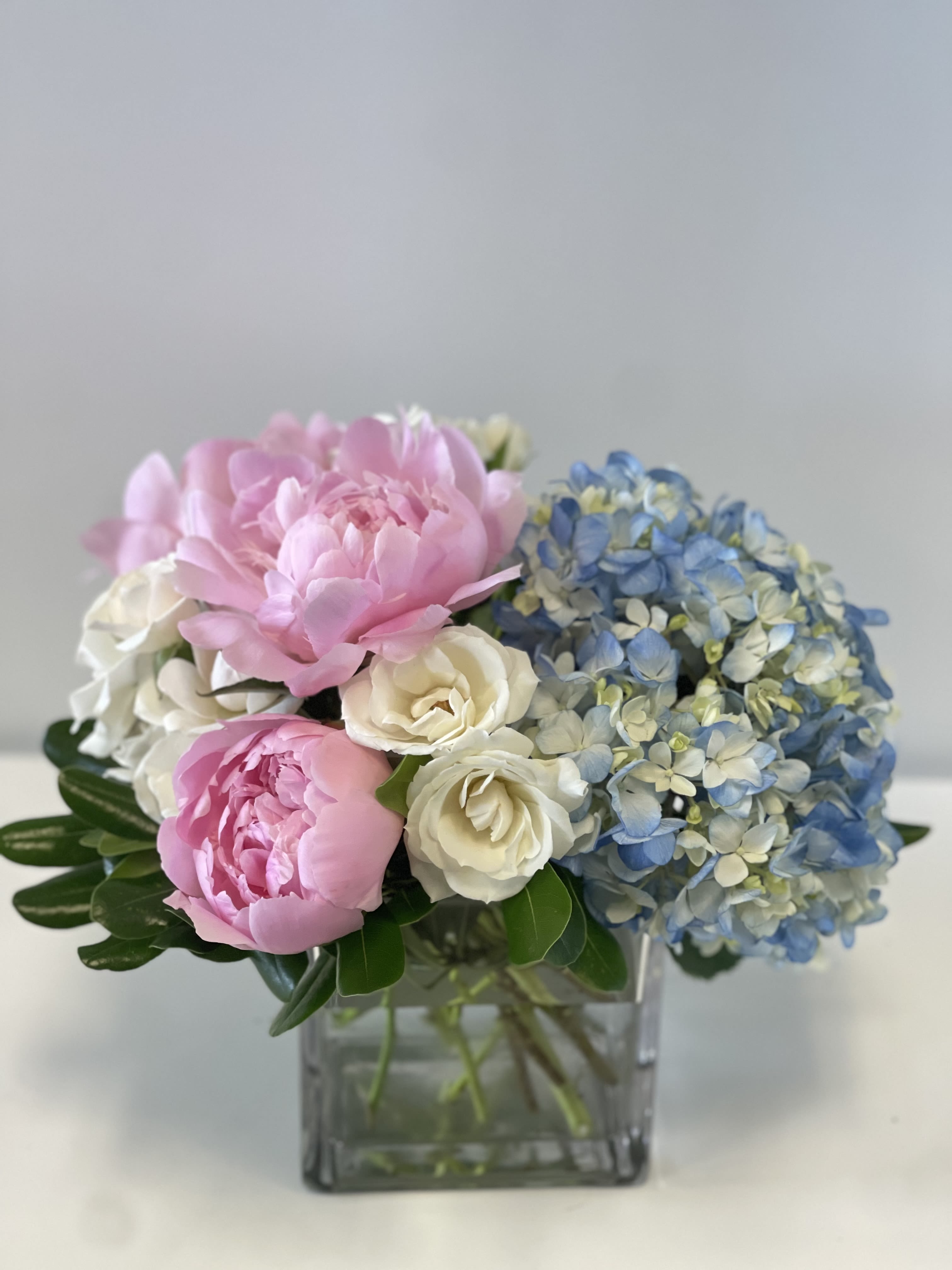 Pink peonies, white roses, and blue hydrangeas in a square glass vase