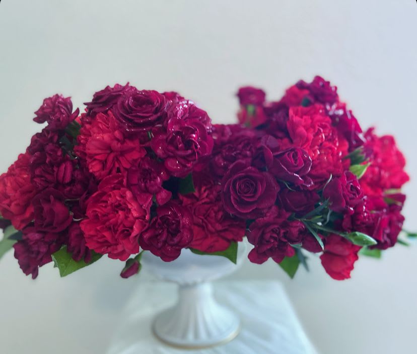 Deep pink and burgundy flower arrangement in a white pedestal vase
