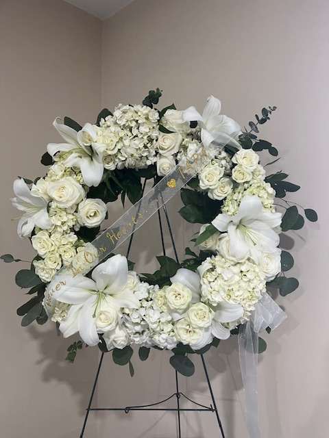 White floral wreath on a stand with lilies and roses