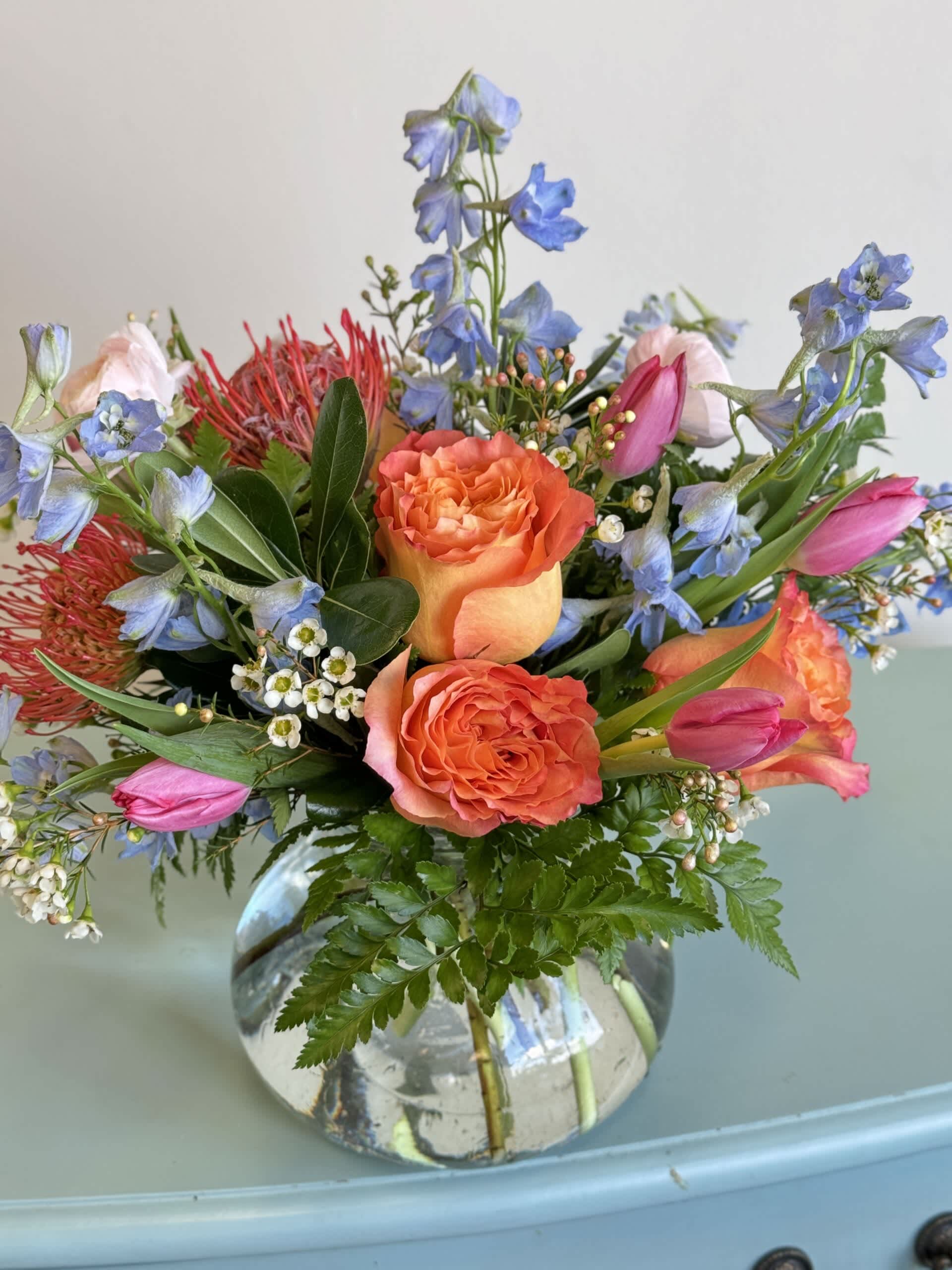 Bouquet of orange roses, pink tulips, and blue flowers in a glass vase