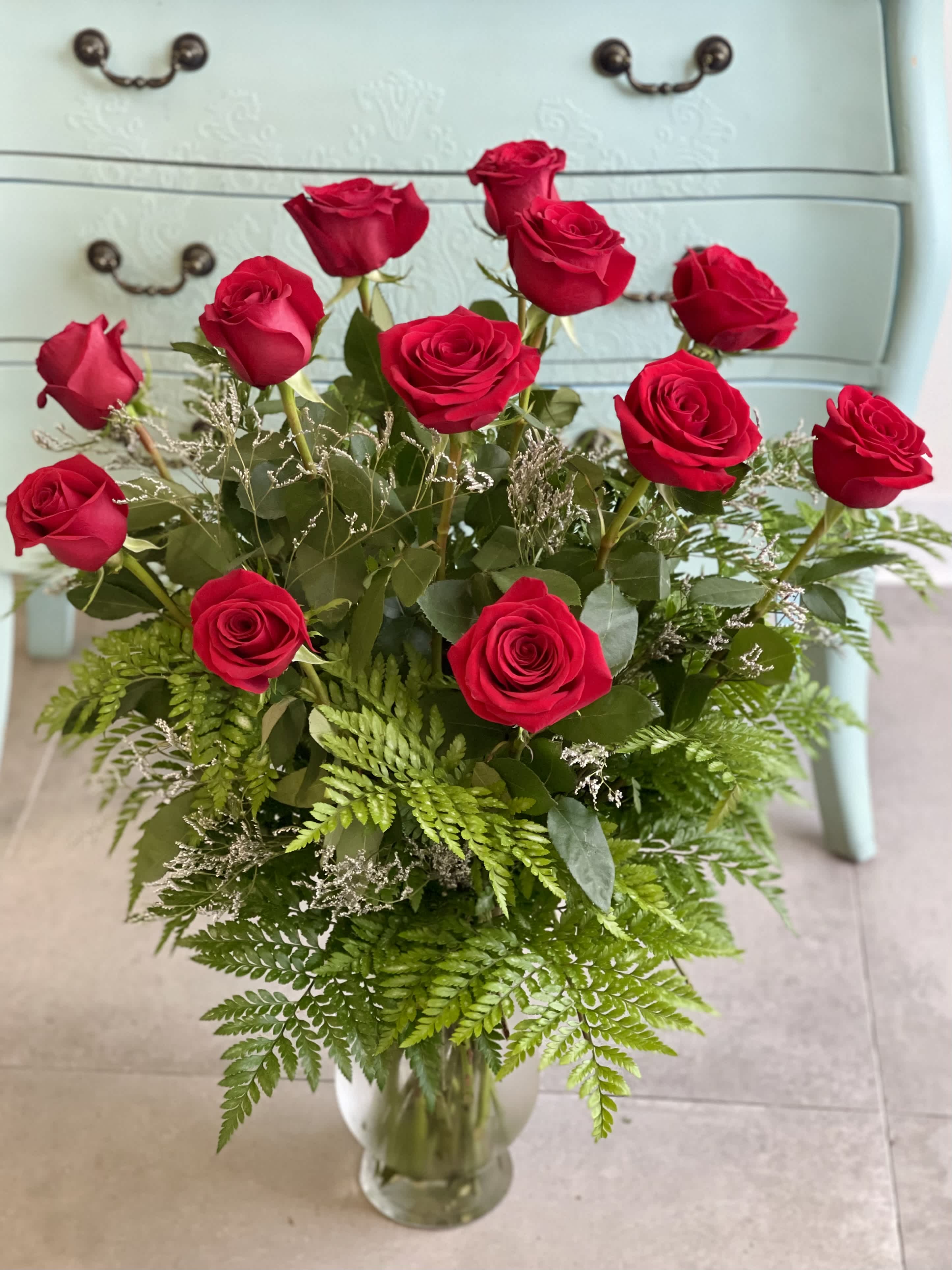 Red roses arranged in a clear glass vase with fern foliage