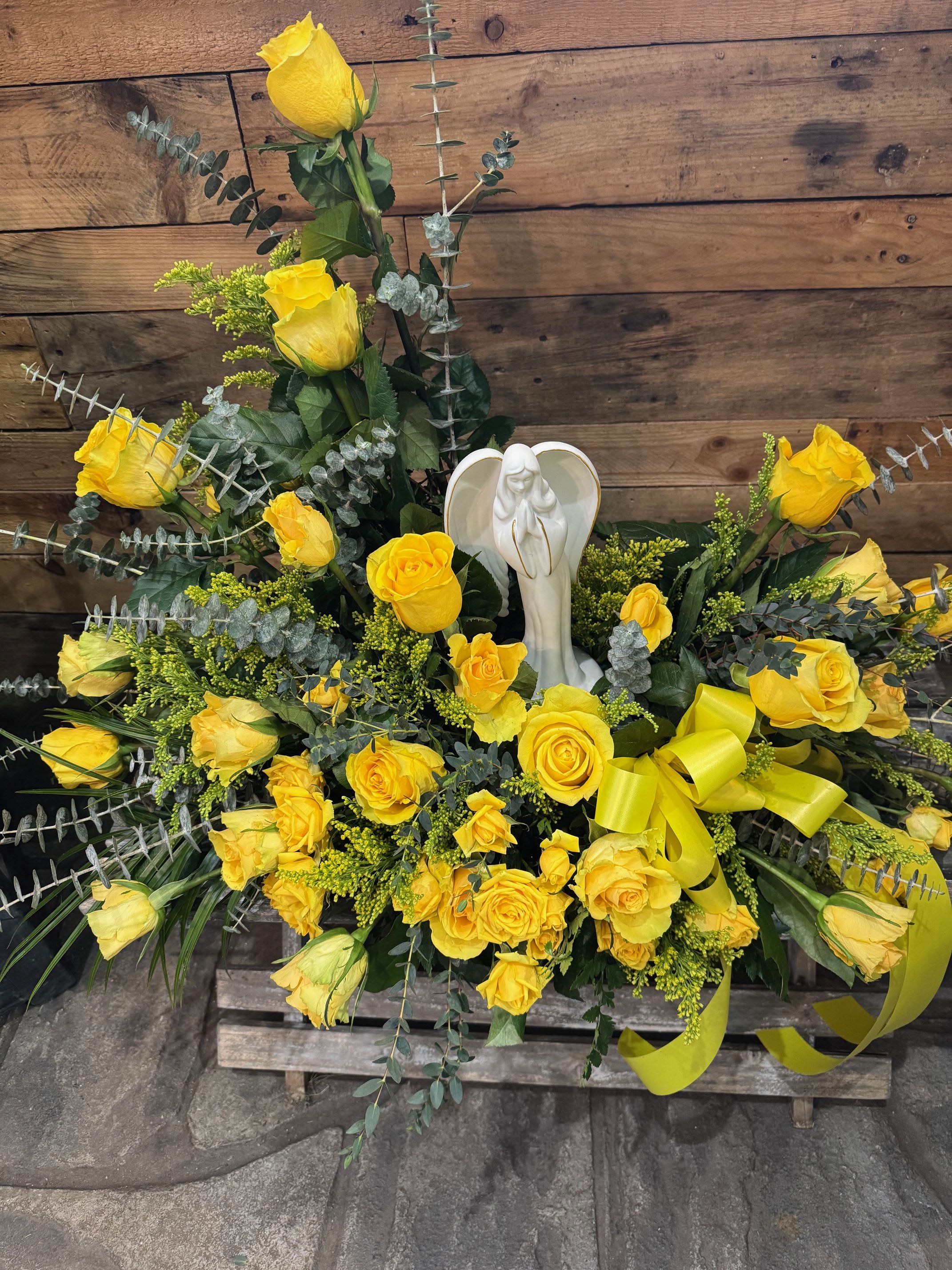 Yellow rose funeral spray with an angel figurine and ribbon