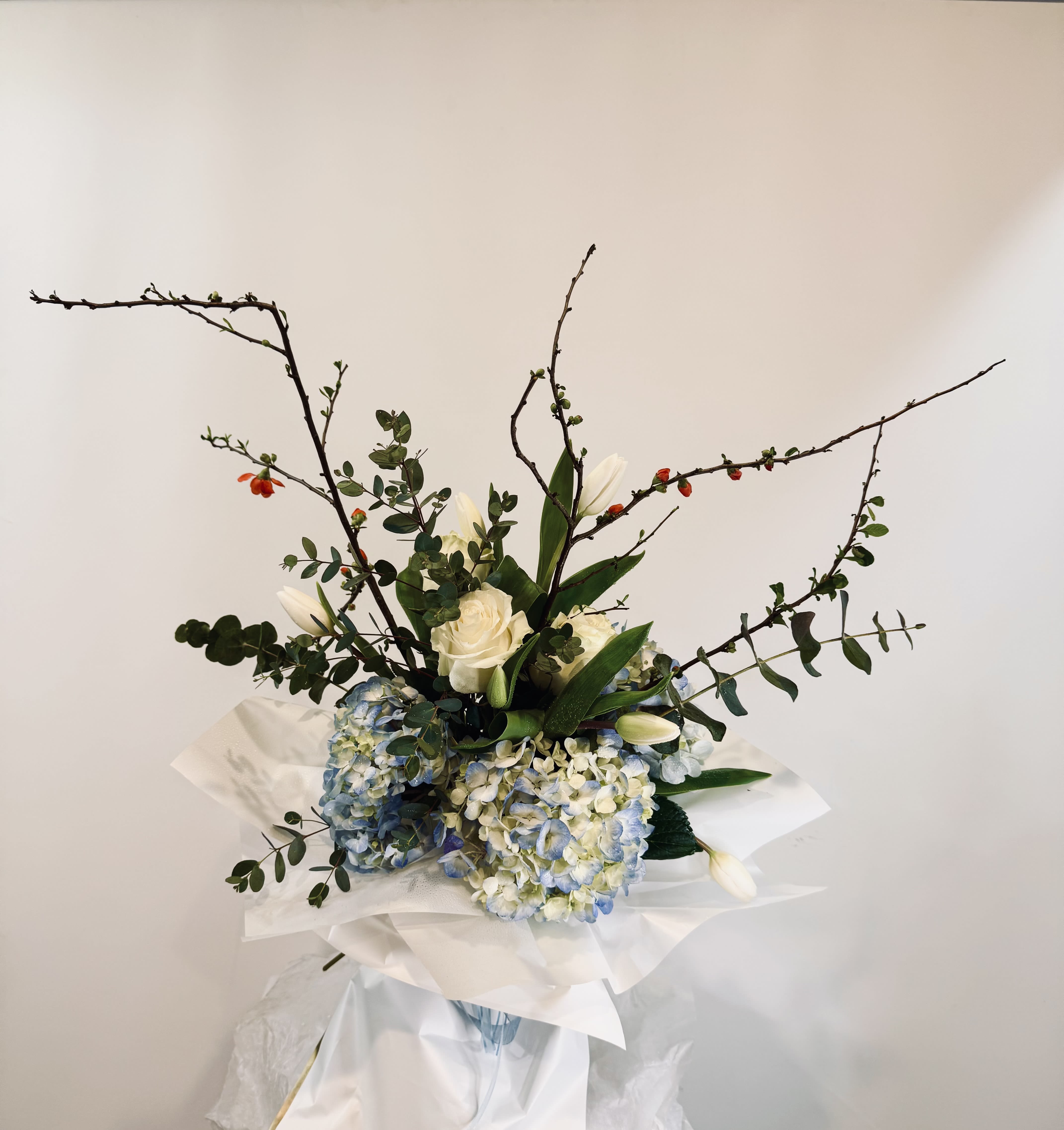 Bouquet of white roses, blue hydrangeas, and white tulips with branching stems