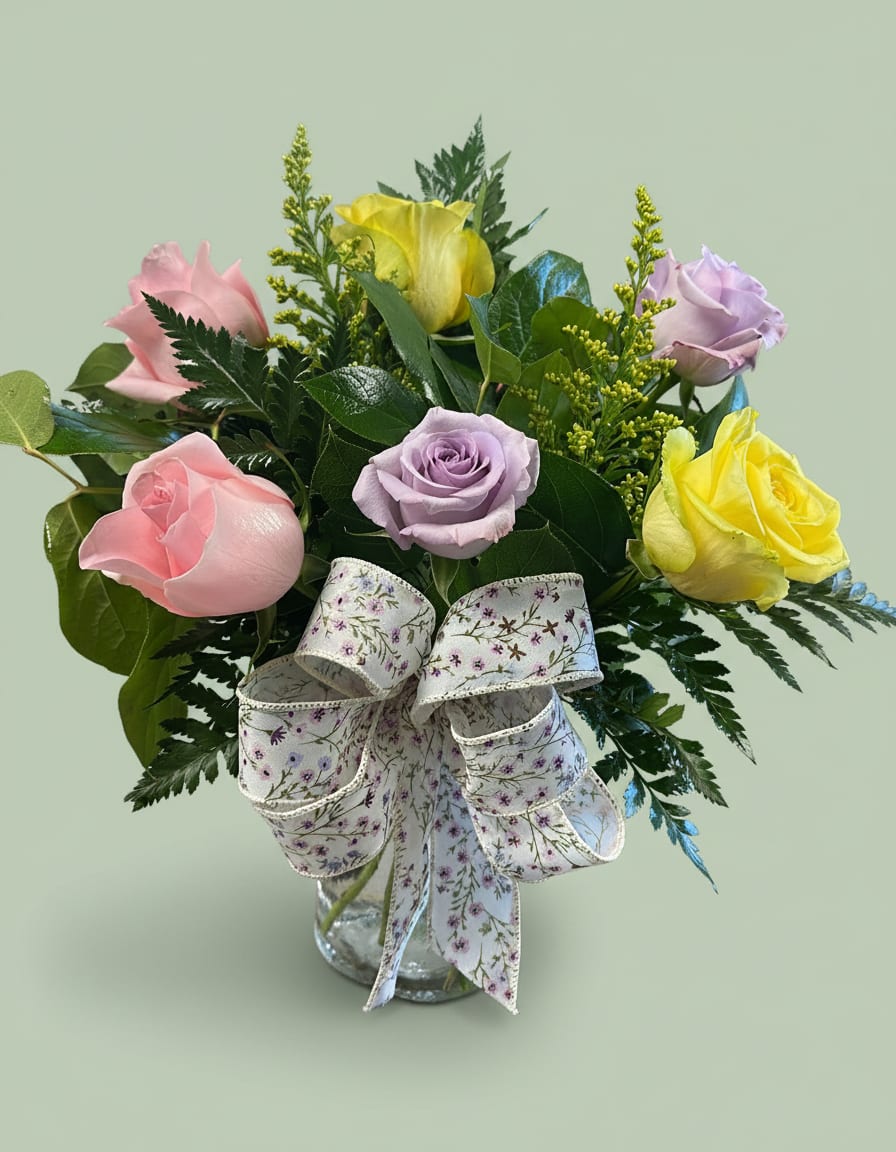 Administrative Professional Special - Cheerful and romantic, this rose arrangement is crafted especially for Administrative Professionals' Week and makes a thoughtful birthday or appreciation gift. A rounded bouquet of soft pink, lavender and bright yellow roses greets the recipient with a sunny, uplifting presence-perfect for saying "thank you" to the person who keeps things running smoothly or for brightening a springtime celebration.  Several roses are gathered tightly and set against dense, dark greenery with airy yellow filler spikes that add height and texture, creating a full, layered silhouette. The stems arrive in a clear glass vase tied with a wide floral-print ribbon for a gift-ready finish; colors read pink, yellow, purple and white in the bloom palette for a fresh, feminine look.  This is the kind of arrangement that will make the person you're honoring feel genuinely seen and appreciated-ideal for an assistant, office manager, receptionist, or anyone who deserves recognition. Standard vase sizing and simple care-fresh water and a cool spot away from direct sun-will keep the roses looking vibrant through the week.