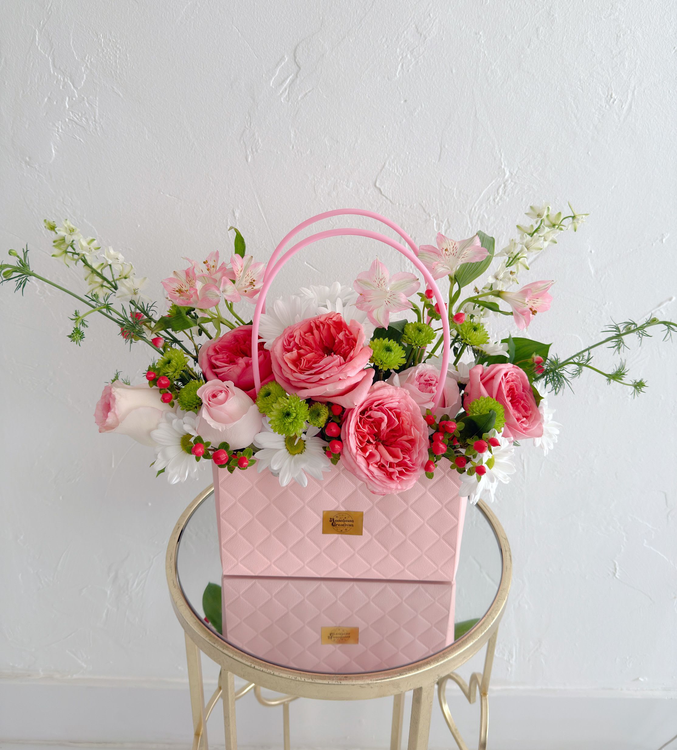 Flowers Bag Ross - Elevate any moment with this sophisticated and charming arrangement. Designed in an elegant pastel pink handbag-style box, it features garden roses in soft pink tones, delicate white blooms, and fresh green accents—creating a harmonious, feminine, and modern composition.  Seasonal flowers and subtle pops of color add texture and movement, making it a visually striking and lively design.  Perfect for birthdays, anniversaries, or to surprise someone with an elegant and memorable gesture. More than flowers, it’s an experience that conveys sweetness, style, and emotion in every detail. 