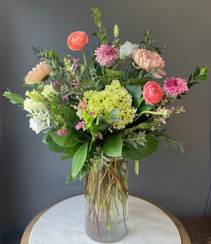 Mixed bouquet of pink, peach, and white flowers in a clear glass vase
