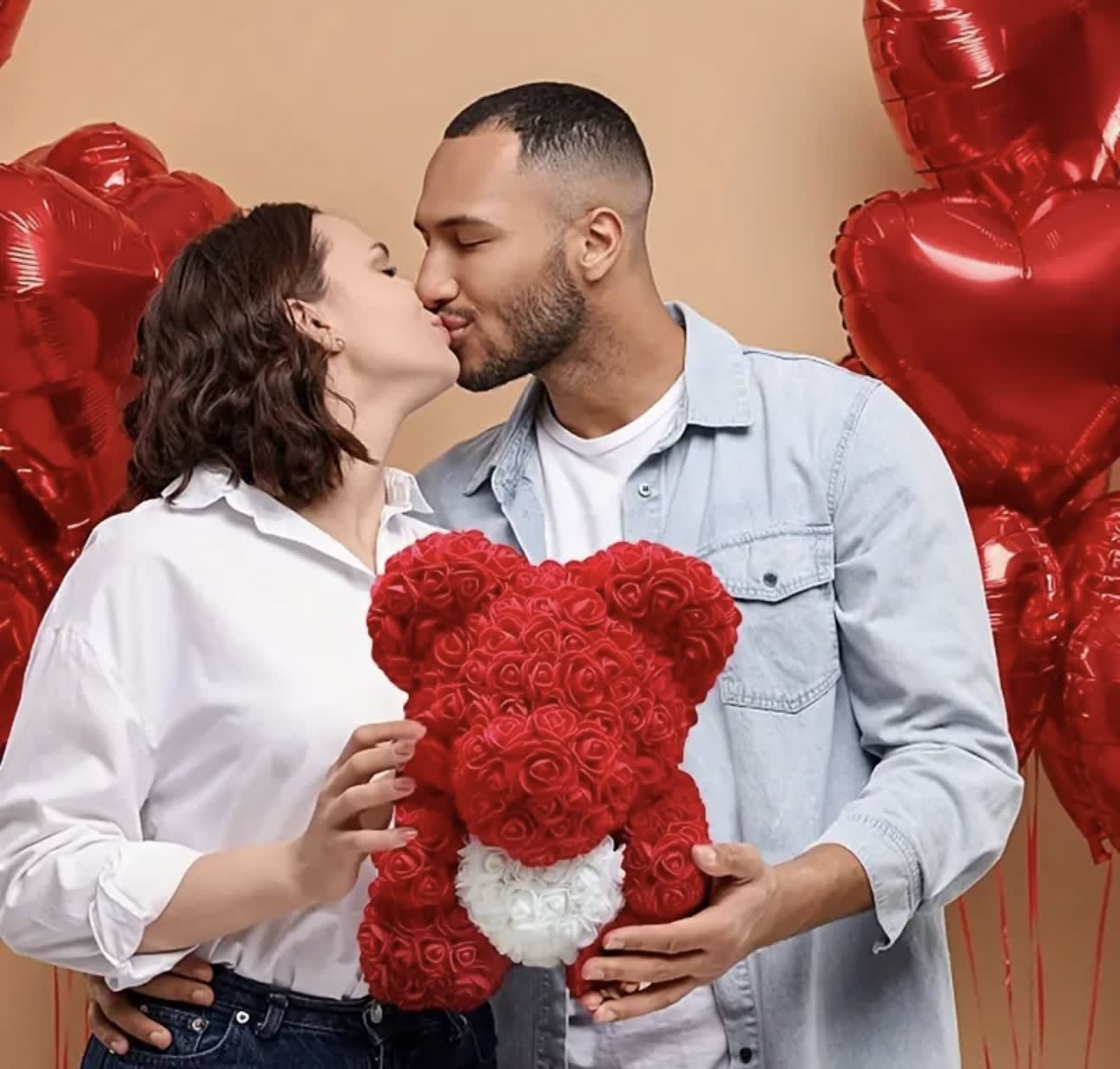 Couple kissing while holding a red rose teddy bear with heart balloons behind them
