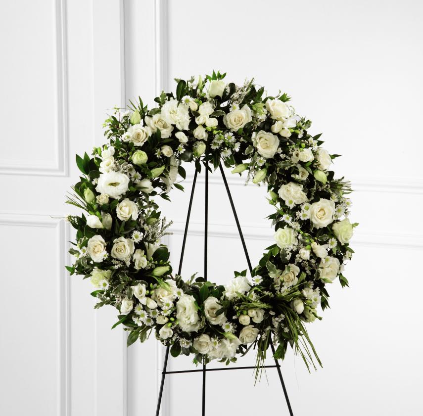 White floral wreath on a black stand with roses and daisies