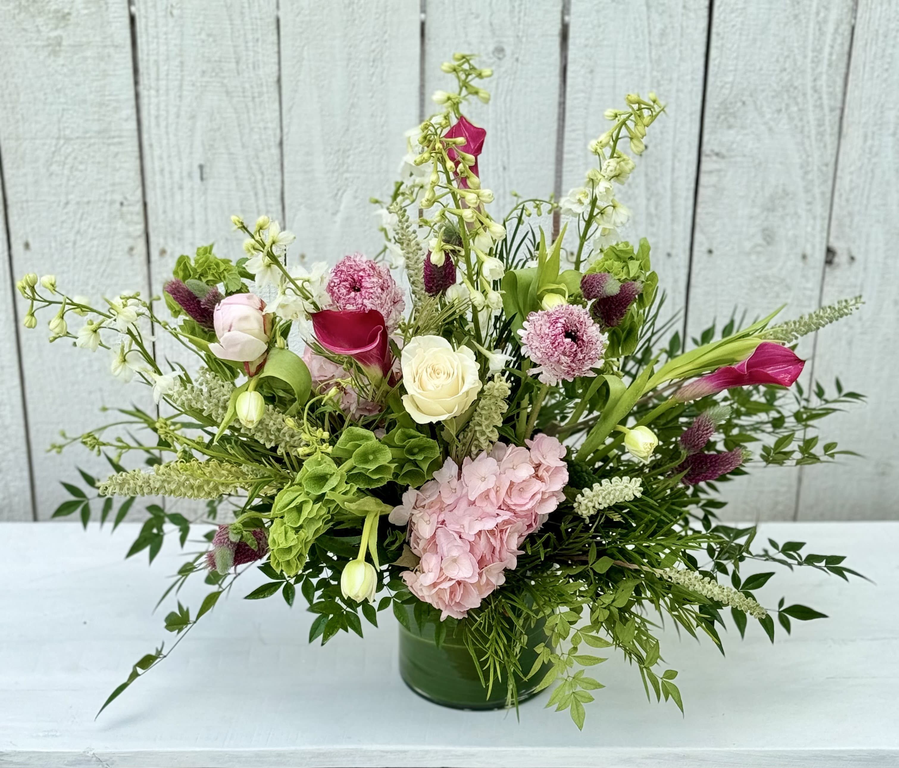 THE ONE &amp; ONLY - A beautiful design of pink flowers, including calla Lilly’s, hydrangeas, ranunculous, fabulous greenery. This one is whimsical and stunning for any table or entryway.
