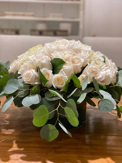 Low arrangement of ivory roses in a round vase with a collar of eucalyptus.