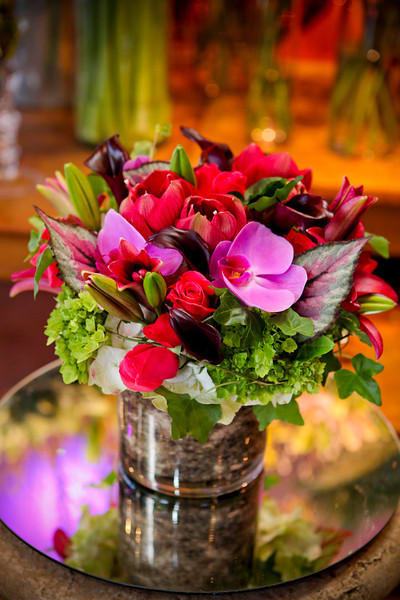 Compact arrangement of pink orchids, red blooms, and green accents in a glass vase on a mirror