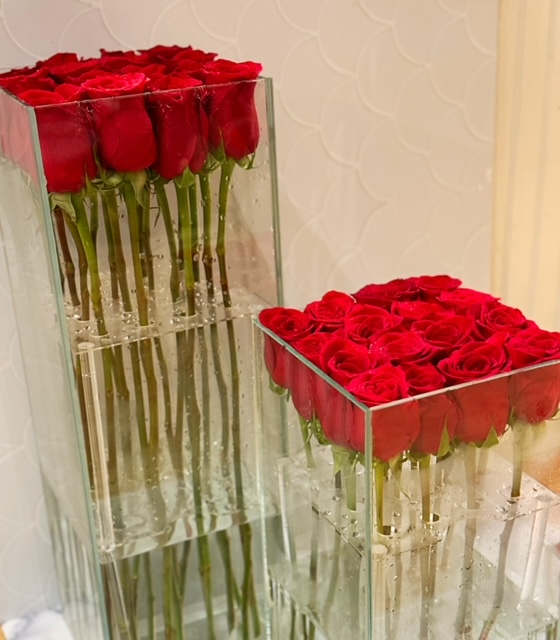 Two clear glass vases filled with tightly packed red roses.