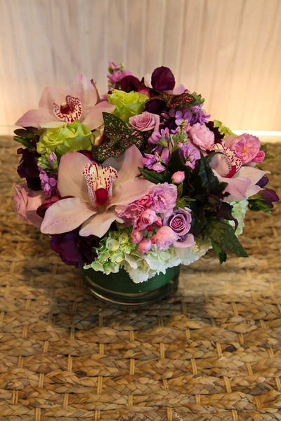Low arrangement of pink orchids, roses, carnations, and hydrangeas in a clear glass vase