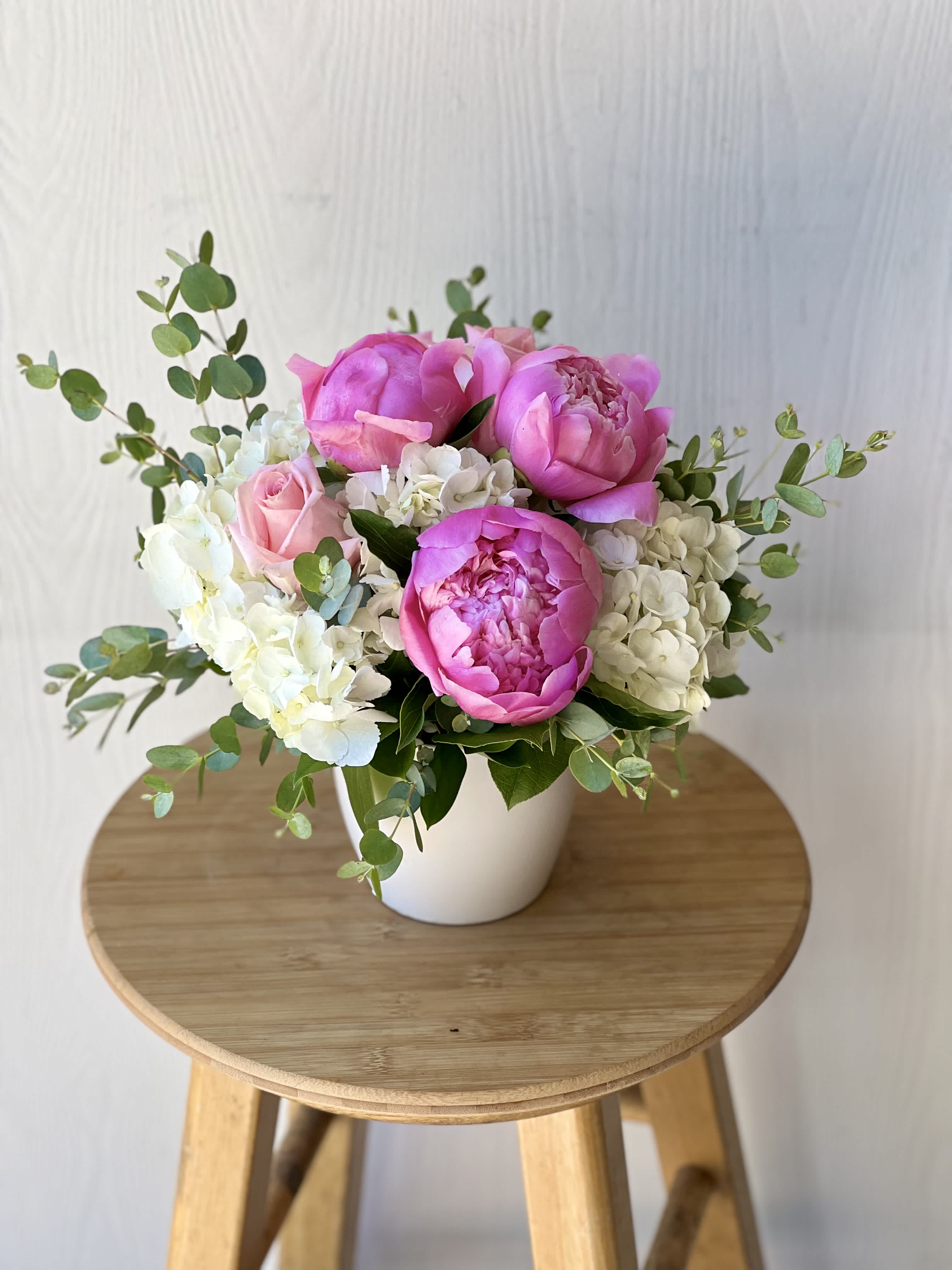 Pink peonies and roses arranged in a white pot