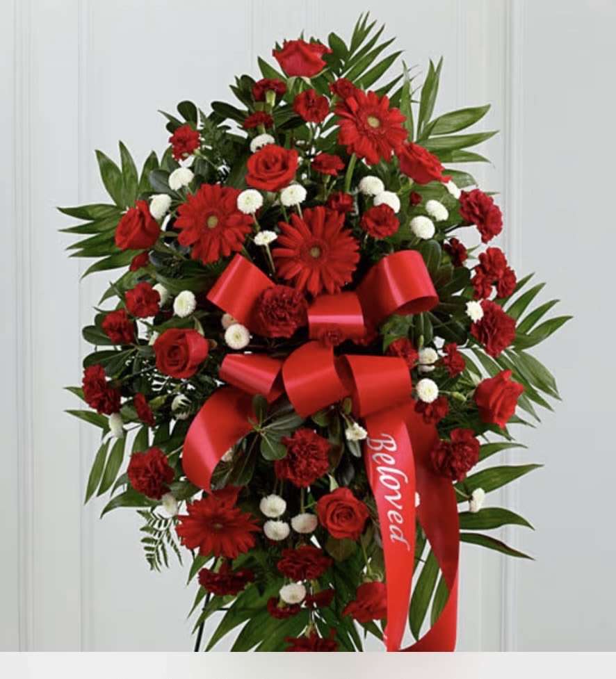 RED STANDING SPRAY  - A striking standing spray featuring rich red roses and vibrant red gerbera daisies, elegantly arranged to convey deep love, respect, and remembrance. The lush blooms are thoughtfully accented with fresh greenery, creating a graceful and balanced display. This heartfelt tribute stands tall, offering a bold expression of sympathy and honor, making it a meaningful choice for memorial services or celebrations of life. 