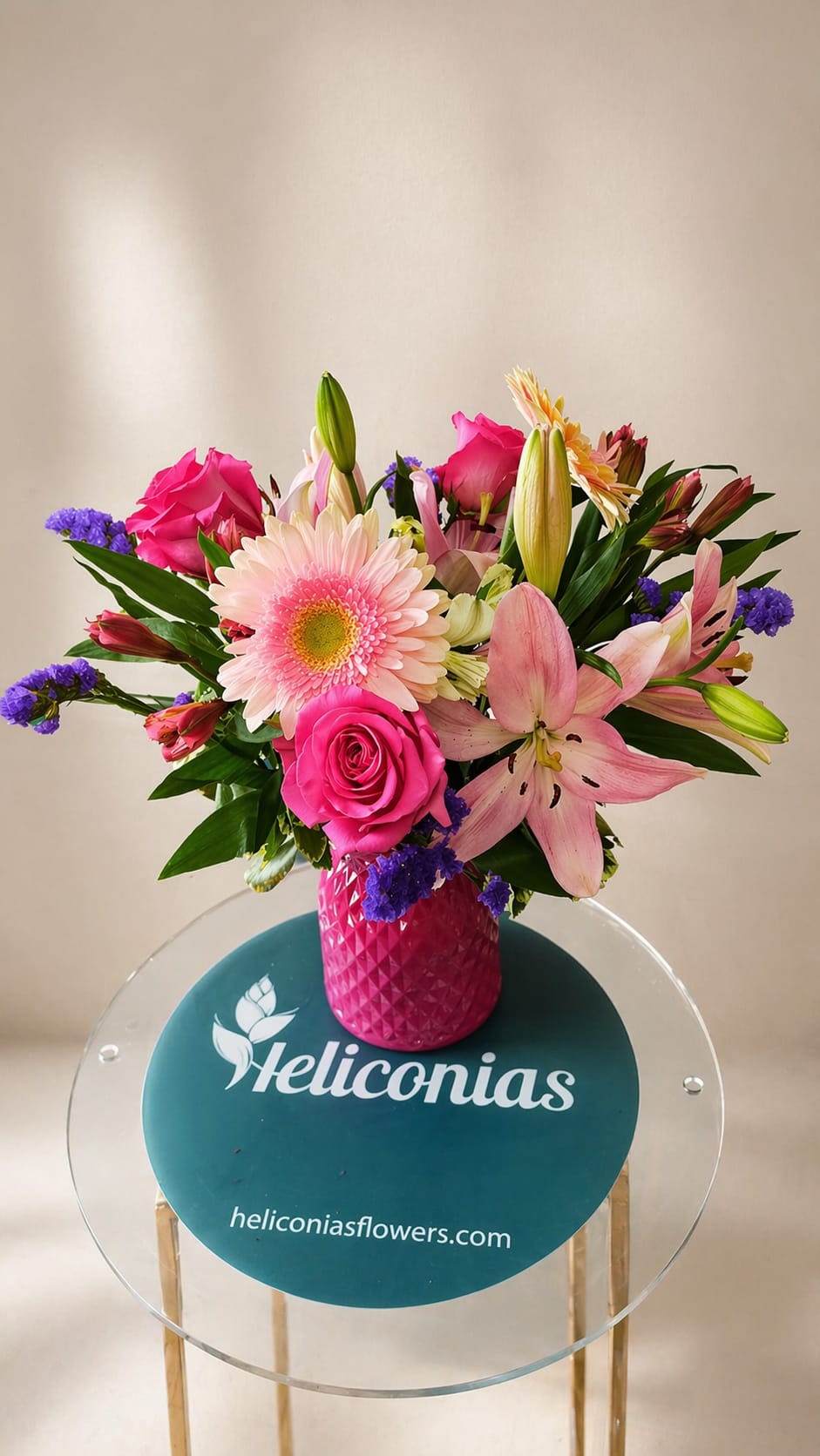 Rosy Dream Vase - Bright, feminine, and full of joyful color, this flower arrangement is a rosy dream for birthdays, thank-you gifts, or romantic occasions. The rounded bouquet centers on bright pink roses and a large pale-pink gerbera daisy that catch the eye first, while pink lilies and sprays of small purple filler flowers add lush texture and a soft, garden-fresh scent. White and yellow accents gently temper the vivid pinks so the overall impression is celebratory without overwhelming.  Arranged compactly in a faceted pink textured vase, the design feels polished and ready to display-no extra styling required. Alongside roses, gerbera, lilies, and alstroemeria, small seasonal blooms provide contrast and movement throughout the piece. The glossy pink vase enhances the palette and gives the arrangement a modern, giftable look that will sit beautifully on a bedside table, office desk, or dining room centerpiece.  Perfect for the person you want to make feel seen and celebrated, this arrangement reads as thoughtful and cheerful whether you're marking a birthday, saying thanks, or sending a romantic note. Packaged to arrive ready-to-enjoy, it's an easy, immediate way to brighten someone's day.