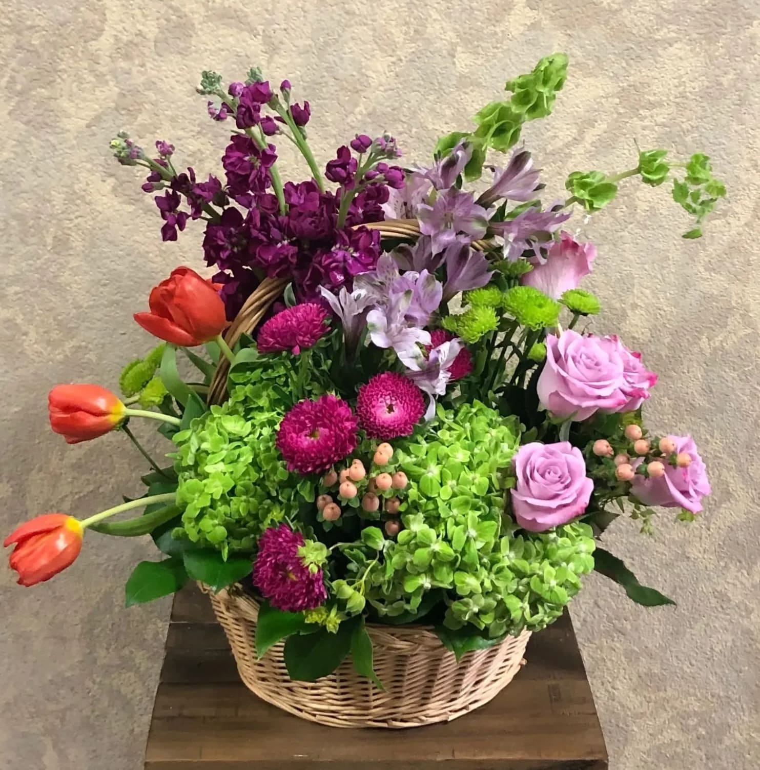 Monet's Gardens, France - Recipe: Purple Stock, Lavender Roses, Orange Tulips, Green Hydrangeas, Purple Alstroemerias, Bells of Ireland, Purple Matsumotos, Green Buttons and Hypericum in a wicker basket. Substitute Available: Yes Design View and Dimensions: Symmetric Front Facing View 10" x 17-20" H Photo shown: Standard