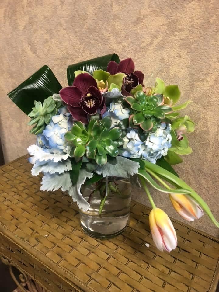Newport, California - Recipe: Blue Hyndrageas, Purple and Green Cymbidium Orchids, Succulents, Dusty Miller, and Leaves in a tall, short vase. Availability: All year round Substitute Available: Yes Design View: Front Symmetric Facing View Photo shown: Regular 