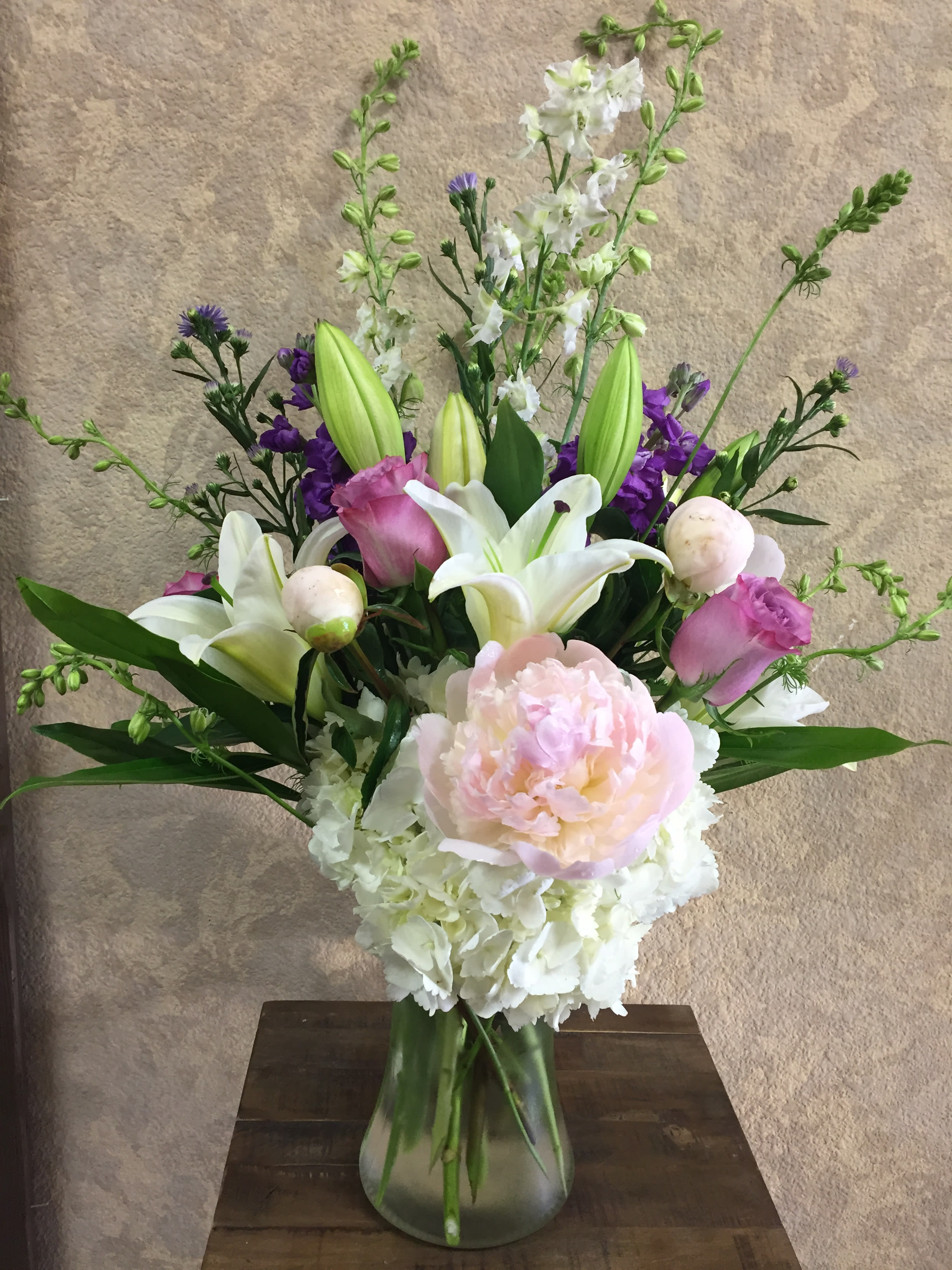 Simple Elegance -   Type of Flowers: An elegant style of White Hydrangeas, Pink Peonies, Purple Roses, Asiatic Lilies, White Delphinium, Purple Stock, and in a tall vase. Availability: Peonies (av: mid-sum-Autumn) Design View: Symmetric Front Facing View Photo shown: Standard 