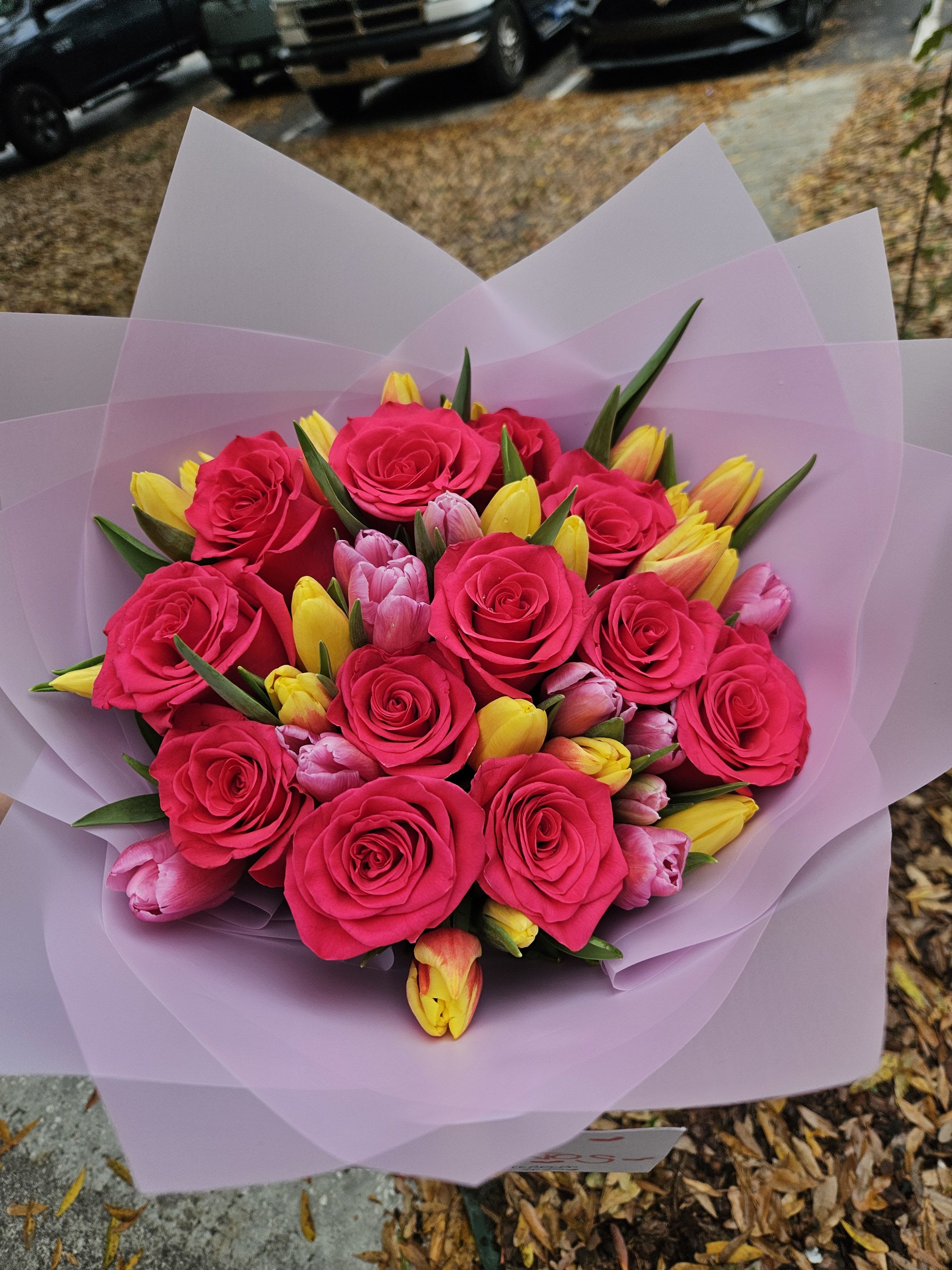Bouquet of hot pink roses and yellow tulips wrapped in pale pink paper
