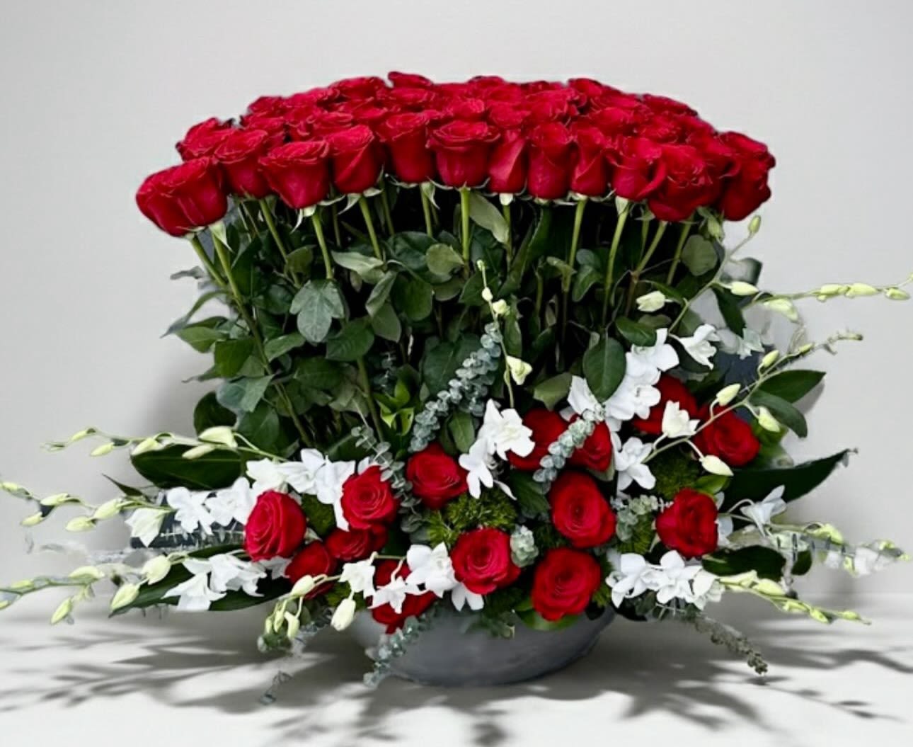 Eternal Love Luxe - A breathtaking luxury arrangement featuring 75 premium red roses, designed in a refined spiral style with fresh eucalyptus accents. Enhanced with delicate white dendrobium orchids, this design blends passion and elegance in perfect harmony—creating a sophisticated and unforgettable floral statement. ️