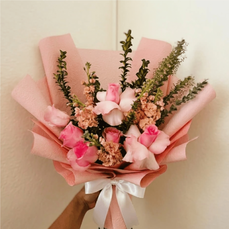 Blushing Love - Soft, romantic, and deeply fragrant—Blushing Love is a timeless tribute to your unique story. This lush arrangement pairs premium light pink roses with the spicy scent of peach stock to create a sensory experience that feels both classic and heartfelt.  This seasonal bouquet features: - Premium Light Pink Roses - Fragrant Peach Stock - Lush Garden Greens  Presentation: Expertly wrapped in our signature textured paper and tied with satin ribbon. Prefer a vase? Add one to your cart to complete the look.   Personal Touch: We’ll include a custom card message with every order. You’ll be able to write your message at checkout.   Please Note: All flowers are subject to seasonal availability. If a specific bloom isn’t available, our designers will thoughtfully substitute with flowers in a similar shape, style, and color.   Standard size shown. Vase upgrade is optional.