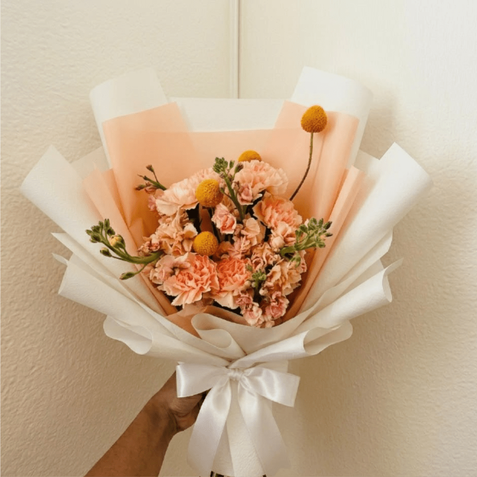 Honey Glow - Radiant, golden, and warm—Honey Glow is a burst of sunshine for your favorite person. This honey-toned arrangement uses peach stock and playful yellow billy buttons to create a look that is both sunny and incredibly sophisticated.  This seasonal bouquet features:  Peach Stock  Peach Carnations  Yellow Billy Buttons  Garden Greens  Presentation: Expertly wrapped in our signature textured paper and tied with satin ribbon. Prefer a vase? Add one to your cart to complete the look.  Personal Touch: We’ll include a custom card message with every order. You’ll be able to write your message at checkout.  Please Note: All flowers are subject to seasonal availability. If a specific bloom isn’t available, our designers will thoughtfully substitute with flowers in a similar shape, style, and color.  Standard size shown. Vase upgrade is optional.   Floral Care Guide  Your arrangement arrives in our signature "double wrap" and is nestled in a protective box. While the stems are secured with a wet wrap for transit they are ready for a full drink!   Unpack: Gently lift the bouquet from the box. Remove the plastic bag and wet towel from the stems. Trim &amp; Hydrate: Trim 1/2" off stems at an angle and place in a clean vase with cool water. Refreshed: Change water daily for a long-lasting bloom. .  