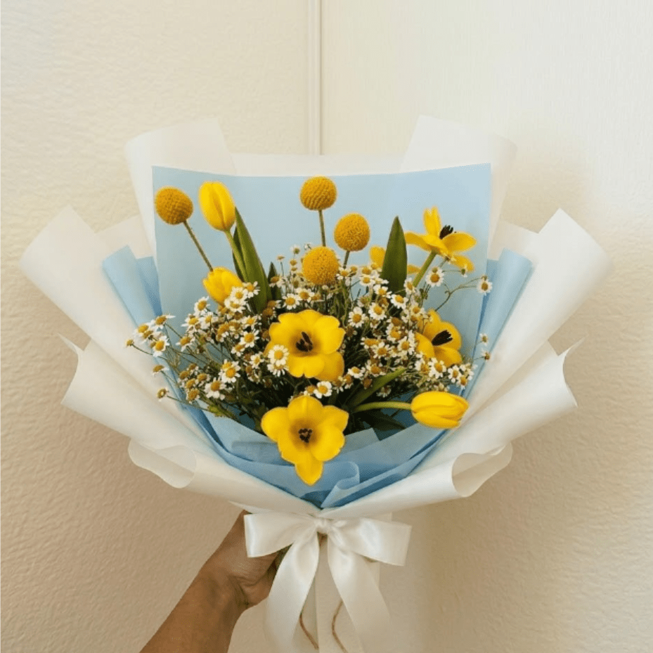 Sunnyside Up - Bright, cheerful, and full of energy—Sunnyside Up is a literal celebration in a wrap. This high-energy arrangement uses yellow tulips and playful billy buttons to bring the joy of a sunny morning directly to their door.  This seasonal bouquet features:  Yellow Tulips  Yellow Billy Buttons  Petite White Feverfew  Garden Greens