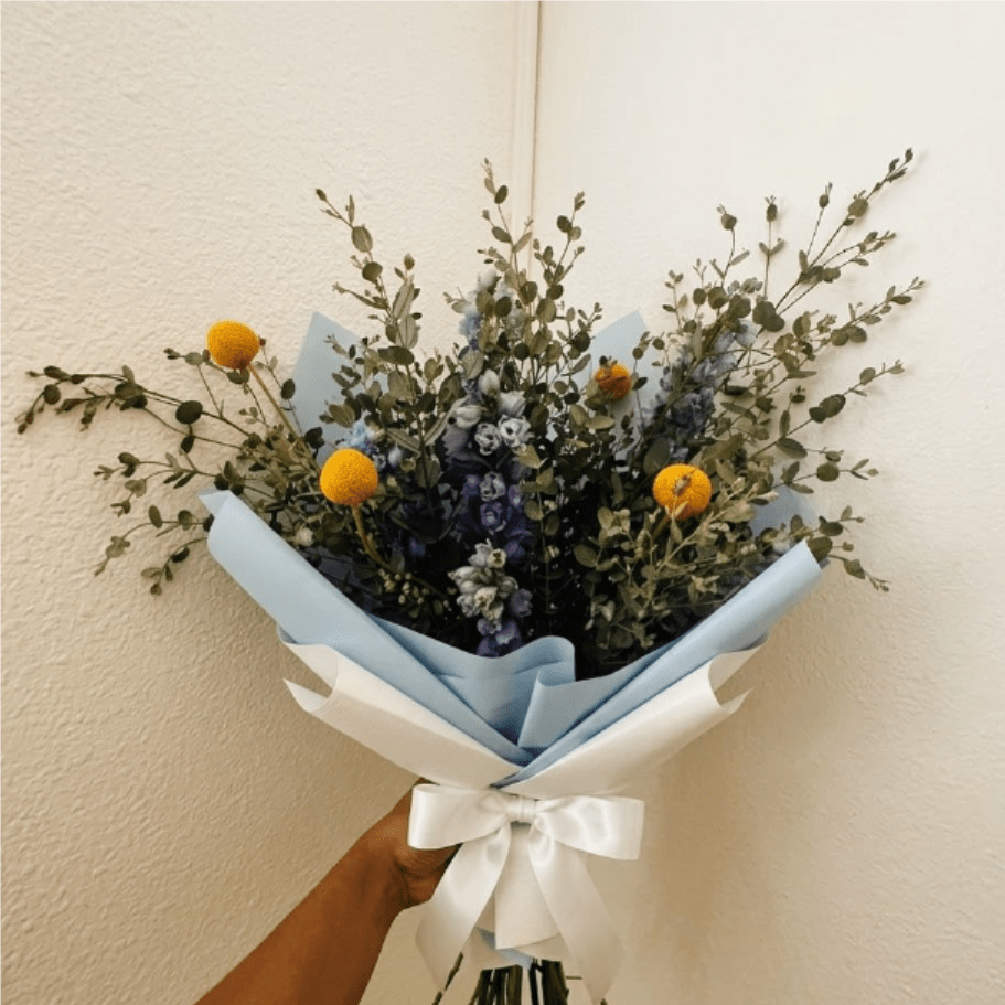 Bright Sky - Modern, bold, and inspiring—Bright Sky is a standout gift for the design-conscious recipient. Sapphire blue delphinium and golden billy buttons create a high-contrast look that feels like a year of clear skies and big dreams.  This seasonal bouquet features:  Light Blue Belladonna Delphinium  Yellow Billy Buttons  Silvery Gunni Eucalyptus  Garden Greens  Presentation: Expertly wrapped in our signature textured paper and tied with satin ribbon. Prefer a vase? Add one to your cart to complete the look.  Personal Touch: We’ll include a custom card message with every order. You’ll be able to write your message at checkout.  Please Note: All flowers are subject to seasonal availability. If a specific bloom isn’t available, our designers will thoughtfully substitute with flowers in a similar shape, style, and color.  Standard size shown. Vase upgrade is optional.   Floral Care Guide  Your arrangement arrives in our signature "double wrap" and is nestled in a protective box. While the stems are secured with a wet wrap for transit they are ready for a full drink!   Unpack: Gently lift the bouquet from the box. Remove the plastic bag and wet towel from the stems. Trim &amp; Hydrate: Trim 1/2" off stems at an angle and place in a clean vase with cool water. Refreshed: Change water daily for a long-lasting bloom.  
