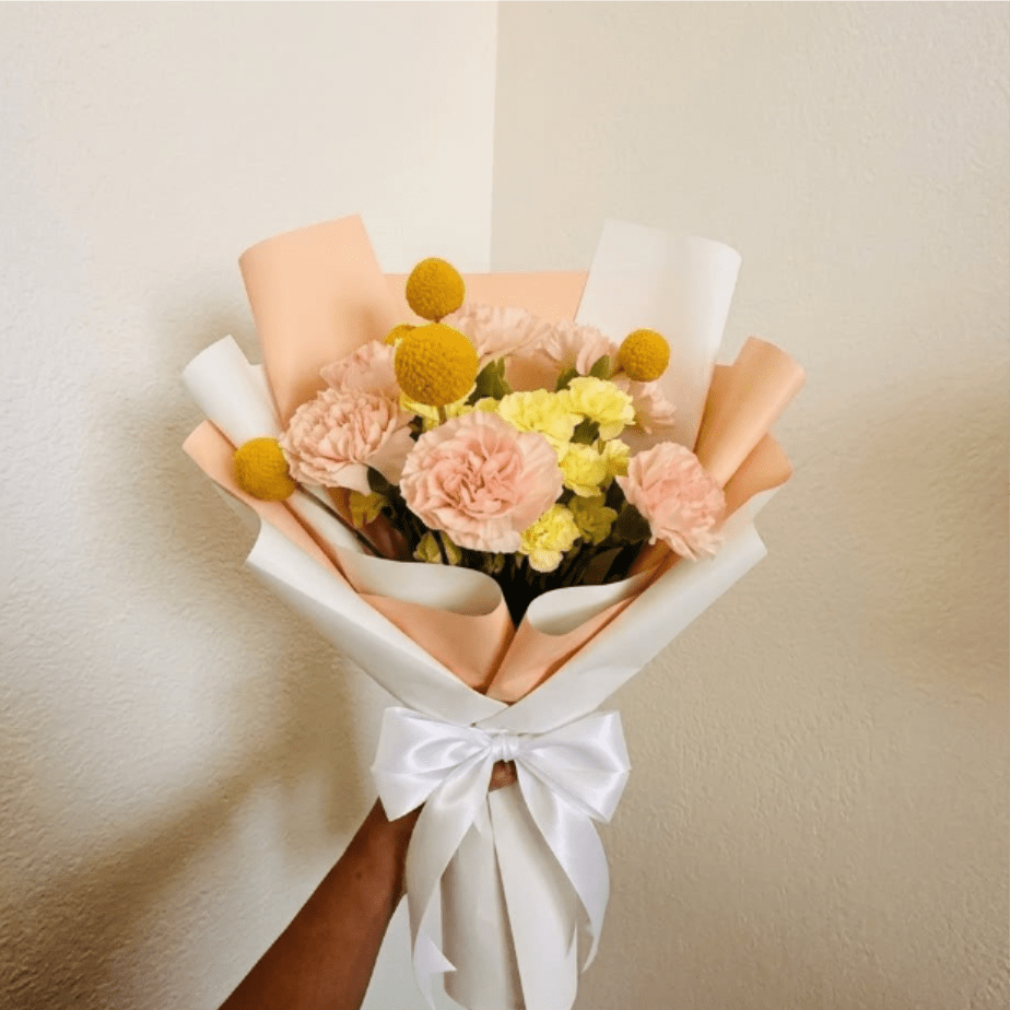 Golden Hour - Radiant, warm, and glowing—Golden Hour captures that perfect late-afternoon light. A mix of peach and yellow tones feels like a warm hug, making it a sophisticated tribute for another year well-lived.  This seasonal bouquet features:  Peach Carnations  Yellow Mini Carnations  Yellow Billy Buttons  Garden Greens  Presentation: Expertly wrapped in our signature textured paper and tied with satin ribbon. Prefer a vase? Add one to your cart to complete the look.  Personal Touch: We’ll include a custom card message with every order. You’ll be able to write your message at checkout.  Please Note: All flowers are subject to seasonal availability. If a specific bloom isn’t available, our designers will thoughtfully substitute with flowers in a similar shape, style, and color.  Standard size shown. Vase upgrade is optional.   Floral Care Guide  Your arrangement arrives in our signature "double wrap" and is nestled in a protective box. While the stems are secured with a wet wrap for transit they are ready for a full drink!   Unpack: Gently lift the bouquet from the box. Remove the plastic bag and wet towel from the stems. Trim &amp; Hydrate: Trim 1/2" off stems at an angle and place in a clean vase with cool water. Refreshed: Change water daily for a long-lasting bloom.  