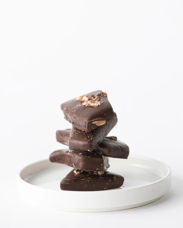 Stack of dark chocolate bark pieces with nuts on a small white plate