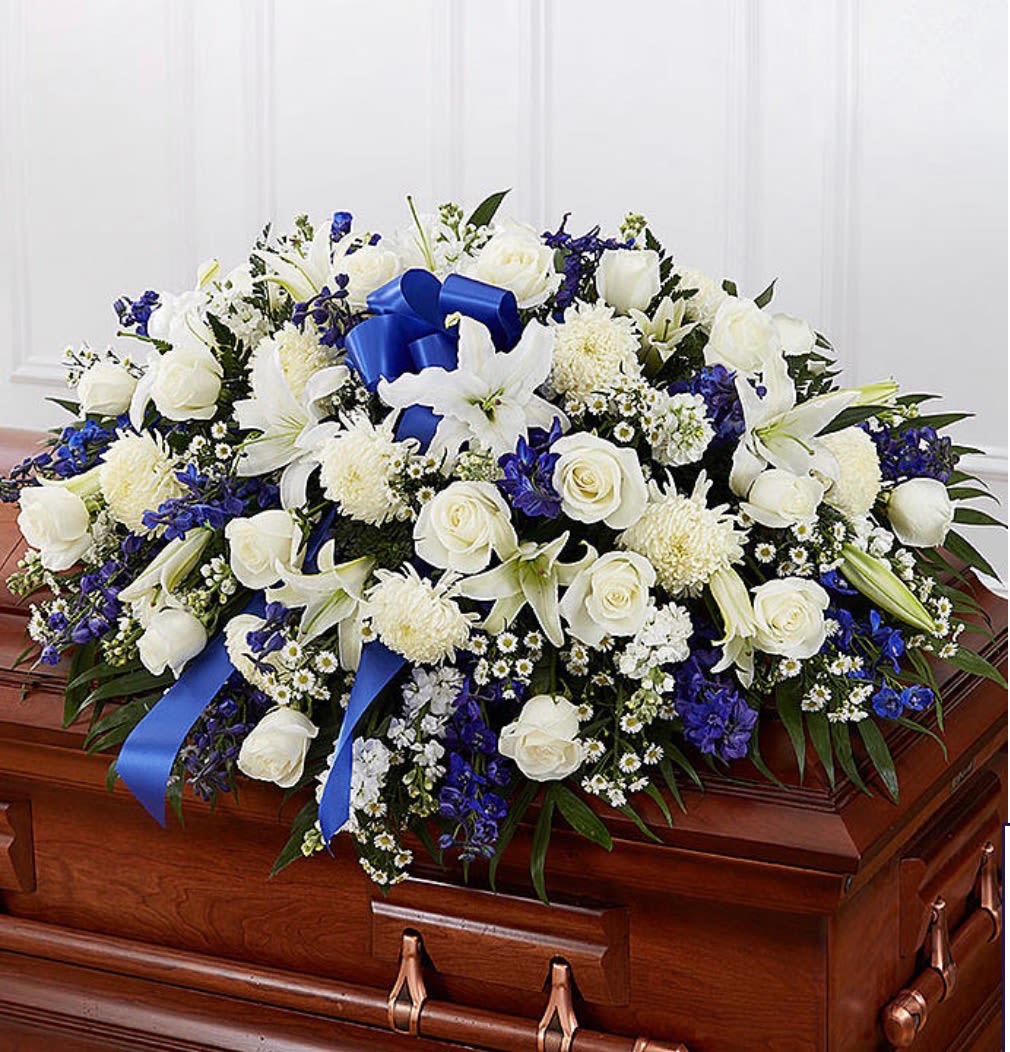 Blue &amp; white casket spray - A delicate and charming casket spray featuring crisp white roses paired with graceful blue delphinium, accented by cheerful white lilies. The soft, velvety petals of the roses create a timeless elegance, while the tall, airy delphinium adds height and a gentle pop of cool blue. Nestled throughout, the daisies bring a fresh, natural touch with their bright centers and simple beauty. Together, these blooms create a serene and uplifting display—perfect for conveying peace, admiration, and a sense of calm sophistication