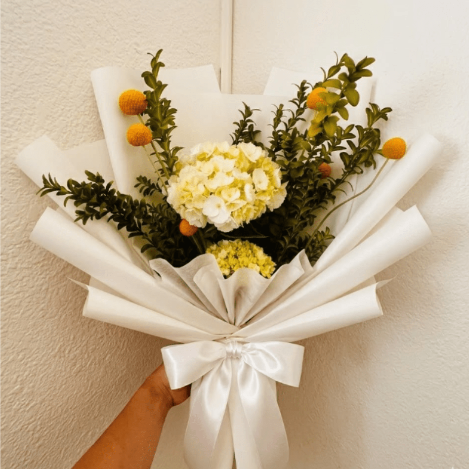 Daybreak - Modern, crisp, and high-contrast—Daybreak celebrates the start of a new, healthier chapter. Pure white hydrangeas and golden billy buttons create a sophisticated, encouraging look for any recovery setting.  This seasonal bouquet features:  White Hydrangea  Yellow Billy Buttons  Fresh Boxwood  Garden Greens  