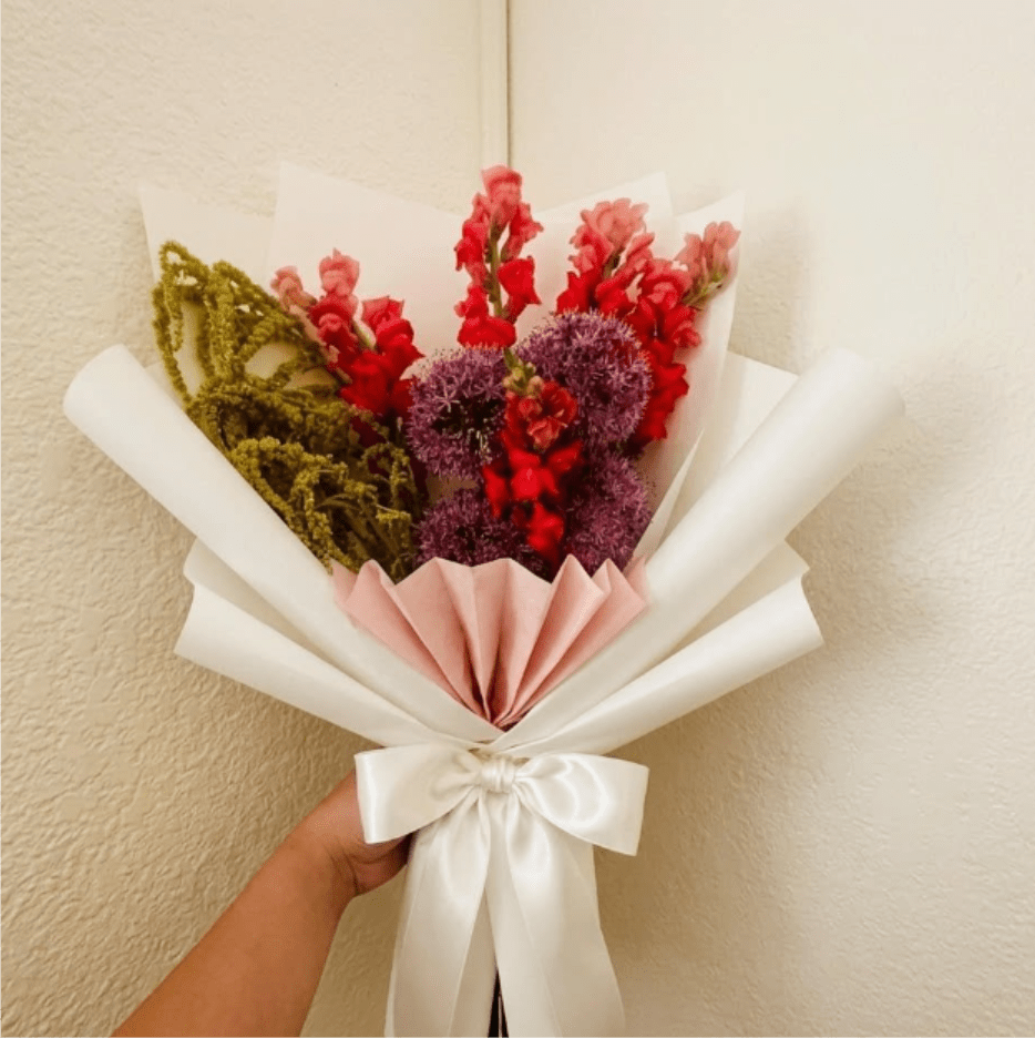 Grand Finale - Dramatic, luxurious, and grand—Grand Finale is a floral standing ovation for life’s biggest wins. Featuring the architectural reach of allium and trailing amaranthus, it is the ultimate "well done" for a major milestone.  This seasonal bouquet features:  Purple Allium  Hot Pink Snapdragons  Green Hanging Amaranthus  Garden Greens  Presentation: Expertly wrapped in our signature textured paper and tied with satin ribbon. Prefer a vase? Add one to your cart to complete the look.  Personal Touch: We’ll include a custom card message with every order. You’ll be able to write your message at checkout.  Please Note: All flowers are subject to seasonal availability. If a specific bloom isn’t available, our designers will thoughtfully substitute with flowers in a similar shape, style, and color.  Standard size shown. Vase upgrade is optional.   Floral Care Guide  Your arrangement arrives in our signature "double wrap" and is nestled in a protective box. While the stems are secured with a wet wrap for transit they are ready for a full drink!   Unpack: Gently lift the bouquet from the box. Remove the plastic bag and wet towel from the stems. Trim &amp; Hydrate: Trim 1/2" off stems at an angle and place in a clean vase with cool water. Refreshed: Change water daily for a long-lasting bloom. 