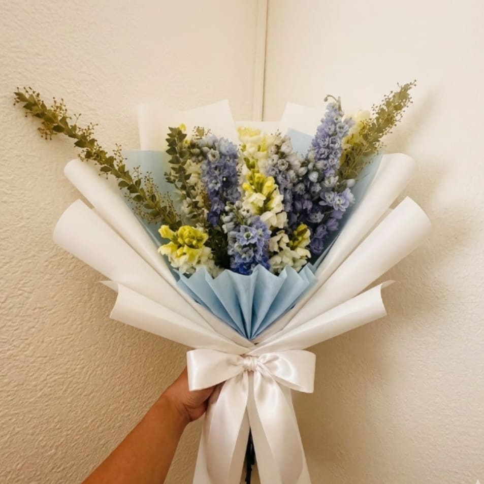 Sapphire Sky - Sophisticated, refined, and memorable—Sapphire Sky is an elegant way to express deep appreciation. The striking sapphire blue of delphinium paired with white snapdragons creates a high-end look that leaves a lasting impression.  This seasonal bouquet features:  Light Blue Belladonna Delphinium  White Snapdragons  Fresh Boxwood  Garden Greens  Presentation: Expertly wrapped in our signature textured paper and tied with satin ribbon. Prefer a vase? Add one to your cart to complete the look.  Personal Touch: We’ll include a custom card message with every order. You’ll be able to write your message at checkout.  Please Note: All flowers are subject to seasonal availability. If a specific bloom isn’t available, our designers will thoughtfully substitute with flowers in a similar shape, style, and color.  Standard size shown. Vase upgrade is optional.   Floral Care Guide  Your arrangement arrives in our signature "double wrap" and is nestled in a protective box. While the stems are secured with a wet wrap for transit they are ready for a full drink!   Unpack: Gently lift the bouquet from the box. Remove the plastic bag and wet towel from the stems. Trim &amp; Hydrate: Trim 1/2" off stems at an angle and place in a clean vase with cool water. Refreshed: Change water daily for a long-lasting bloom. 