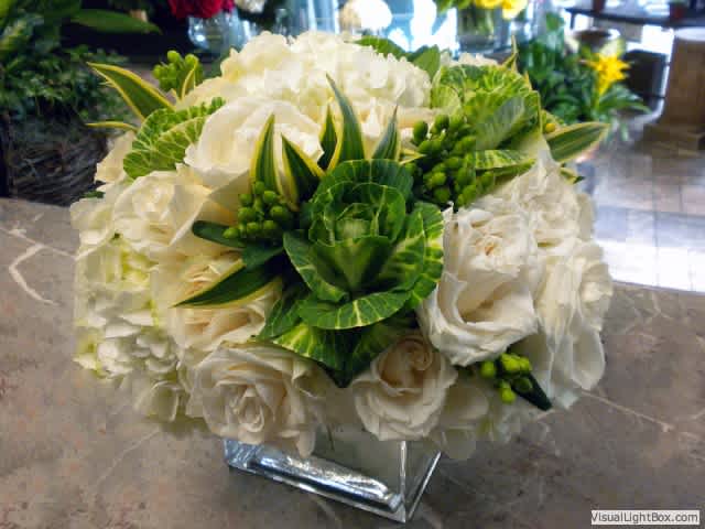 White rose bouquet with green variegated foliage in a square vase
