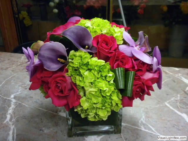 Bouquet of red roses, purple calla lilies, and green hydrangeas in a glass vase