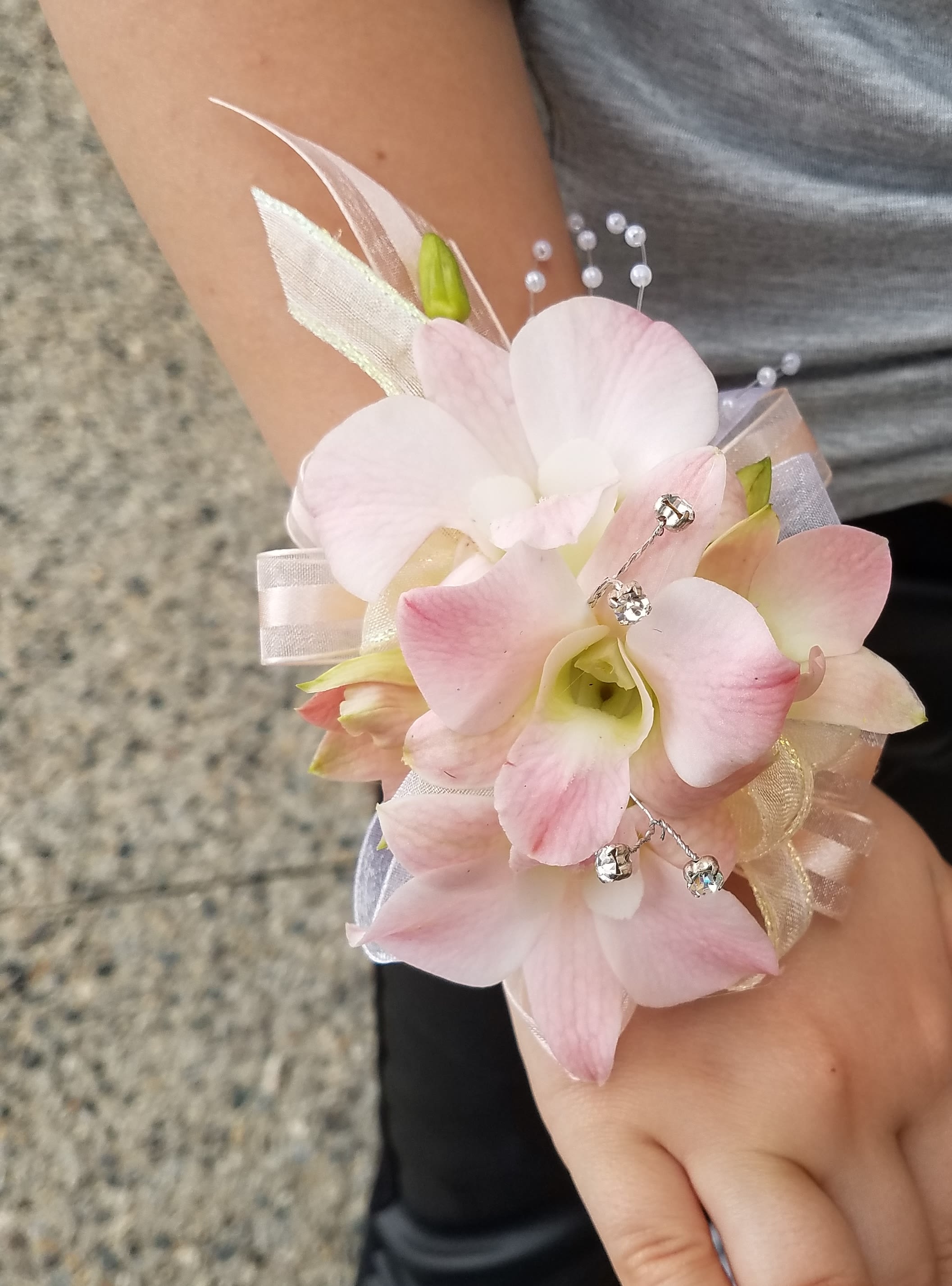 Blush Orchid Wrist Corsage - A delicate and romantic wrist corsage featuring soft blush orchids, elegant ribbon accents, and subtle decorative details.  Designed for bridesmaids, mothers, or special guests, this piece adds a graceful and feminine touch to any wedding look. Lightweight and comfortable, each corsage is handcrafted for a refined and polished finish.