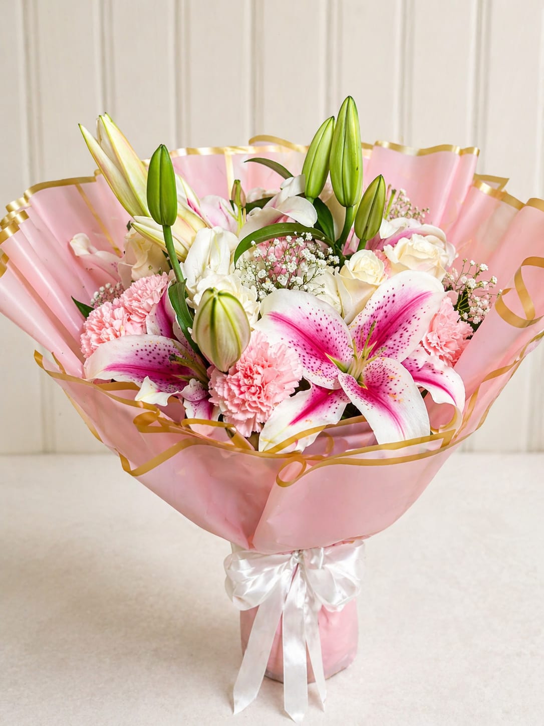 Blush lily elegance bouquet  - A soft and romantic hand-tied bouquet featuring pink stargazer lilies, white roses, blush carnations, and delicate baby’s breath, wrapped in premium pink paper with gold trim and finished with a satin bow. Perfect for birthdays, anniversaries, or a sweet, elegant gift.
