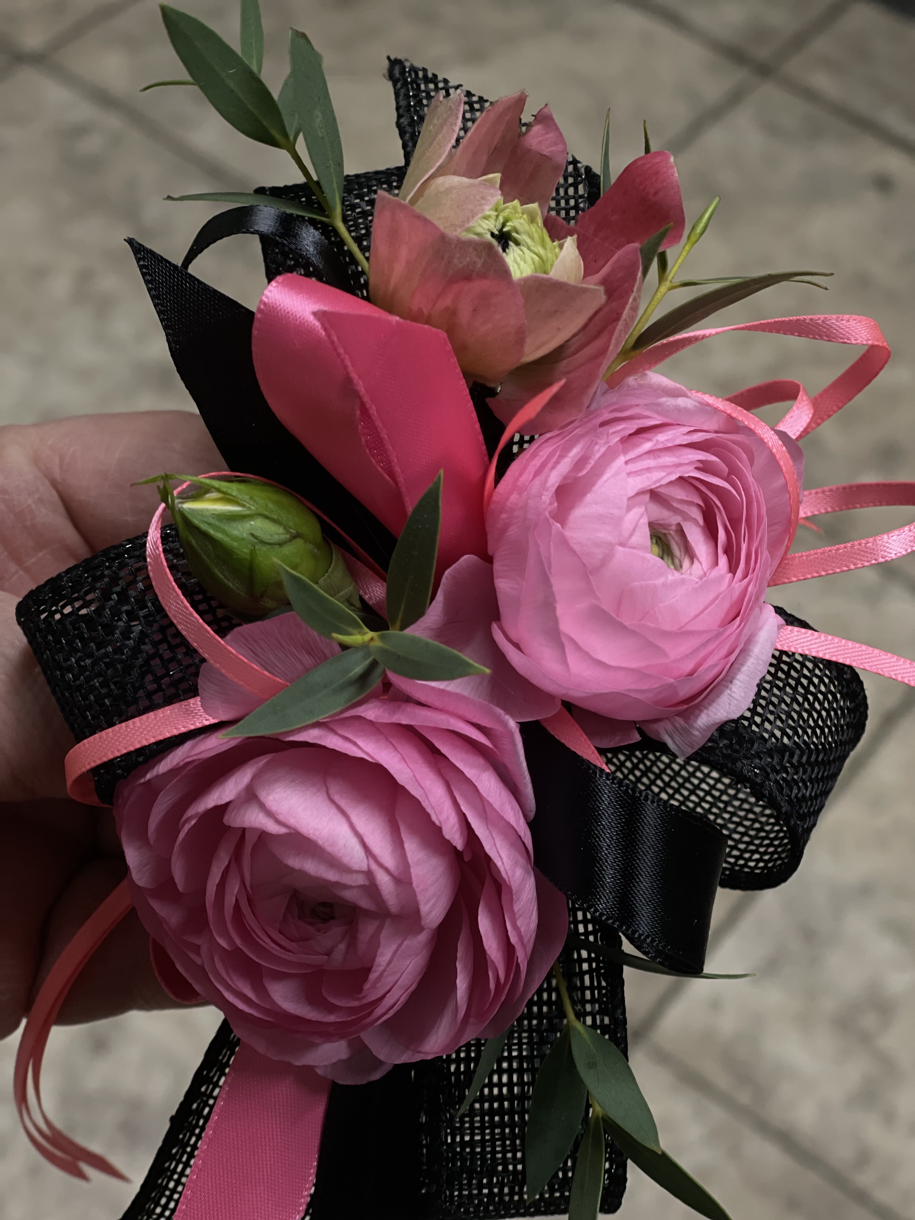 Bold Pink Wrist Corsage  - A bold and stylish wrist corsage featuring vibrant pink ranunculus, delicate accent blooms, and modern ribbon detailing.  Designed with a striking contrast of soft florals and black accents, this corsage is perfect for prom, weddings, or special occasions where you want to stand out.  Lightweight and comfortable to wear, it adds a fashionable floral touch to any look.  Each corsage is handcrafted and may vary slightly while maintaining the same color palette and style.