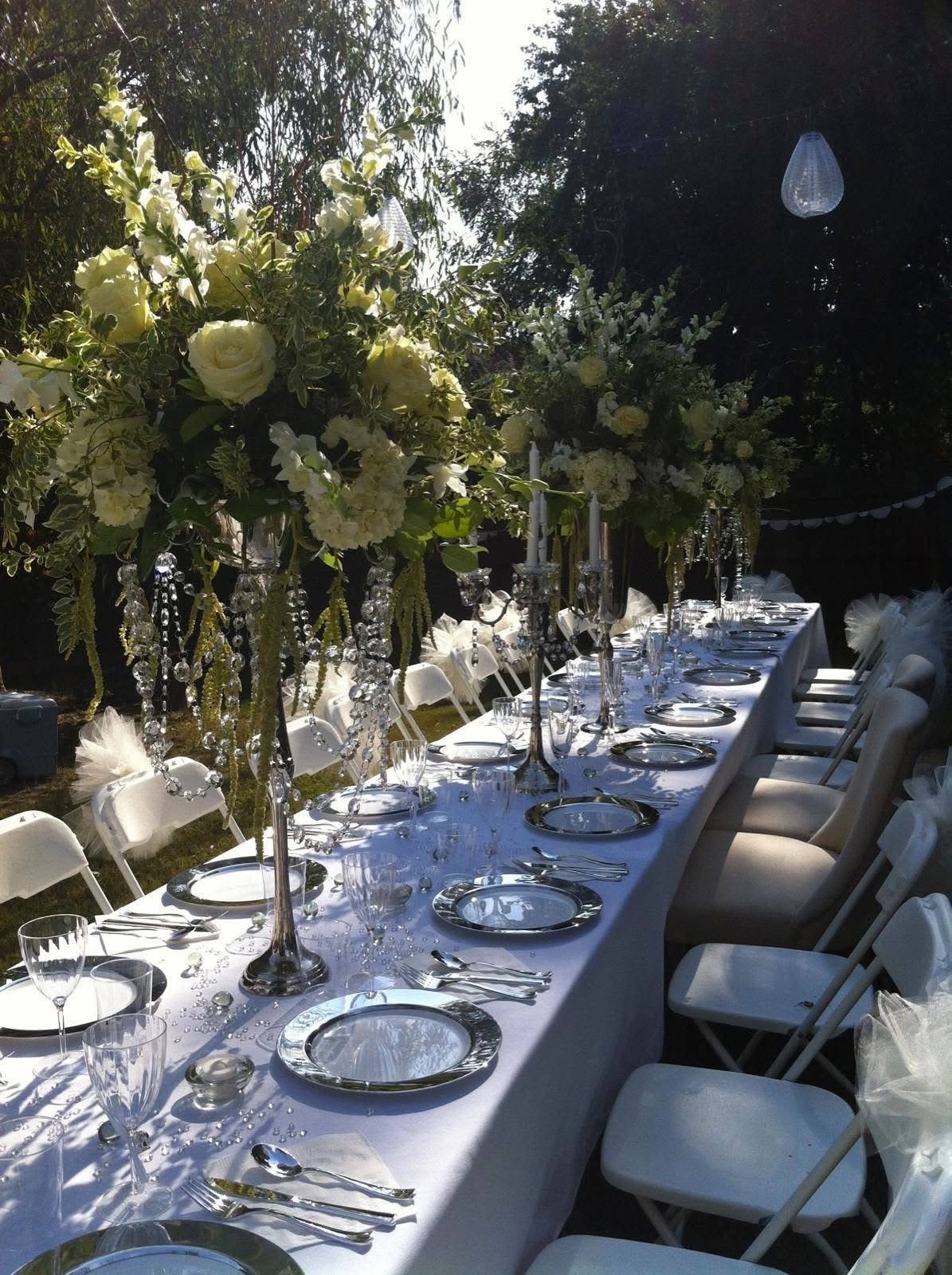     Classic Garden Wedding Tablescape - Create an unforgettable wedding atmosphere with our luxury floral table designs.  This elegant setup features lush white blooms, soft greenery, and tall statement centerpieces accented with crystal details for a timeless and sophisticated look.  Perfect for weddings, receptions, and upscale events, each design is fully customized to match your vision, venue, and color palette.  We offer full-service floral styling including centerpieces, table décor, and event setup.  Please contact us for a personalized consultation and custom quote.