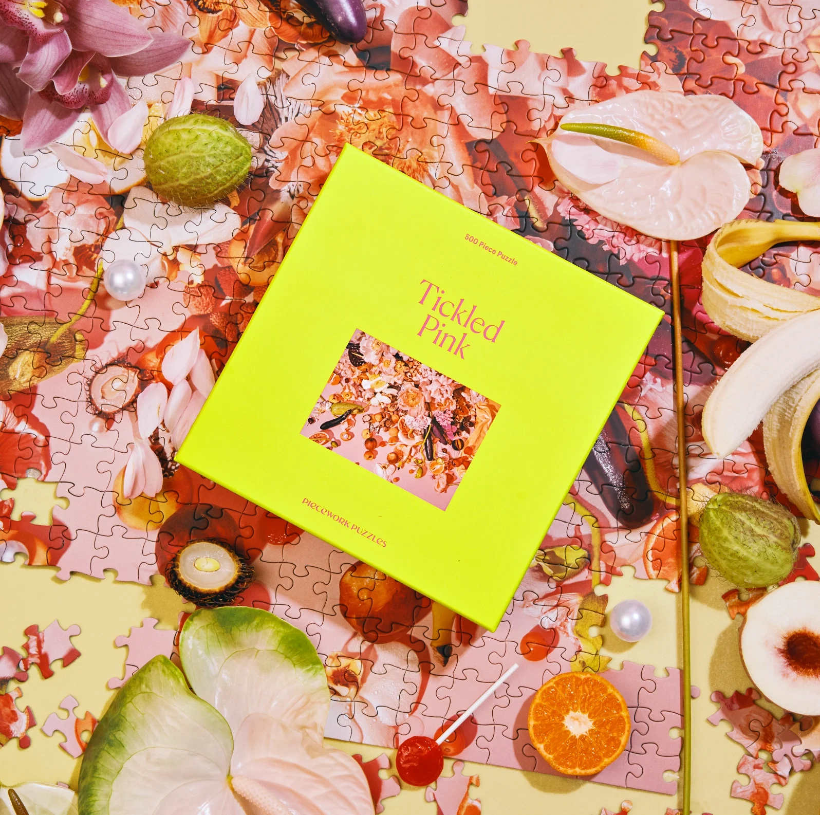 Bright yellow 'Tickled Pink' 500-piece puzzle box on a floral puzzle with scattered fruits and flowers