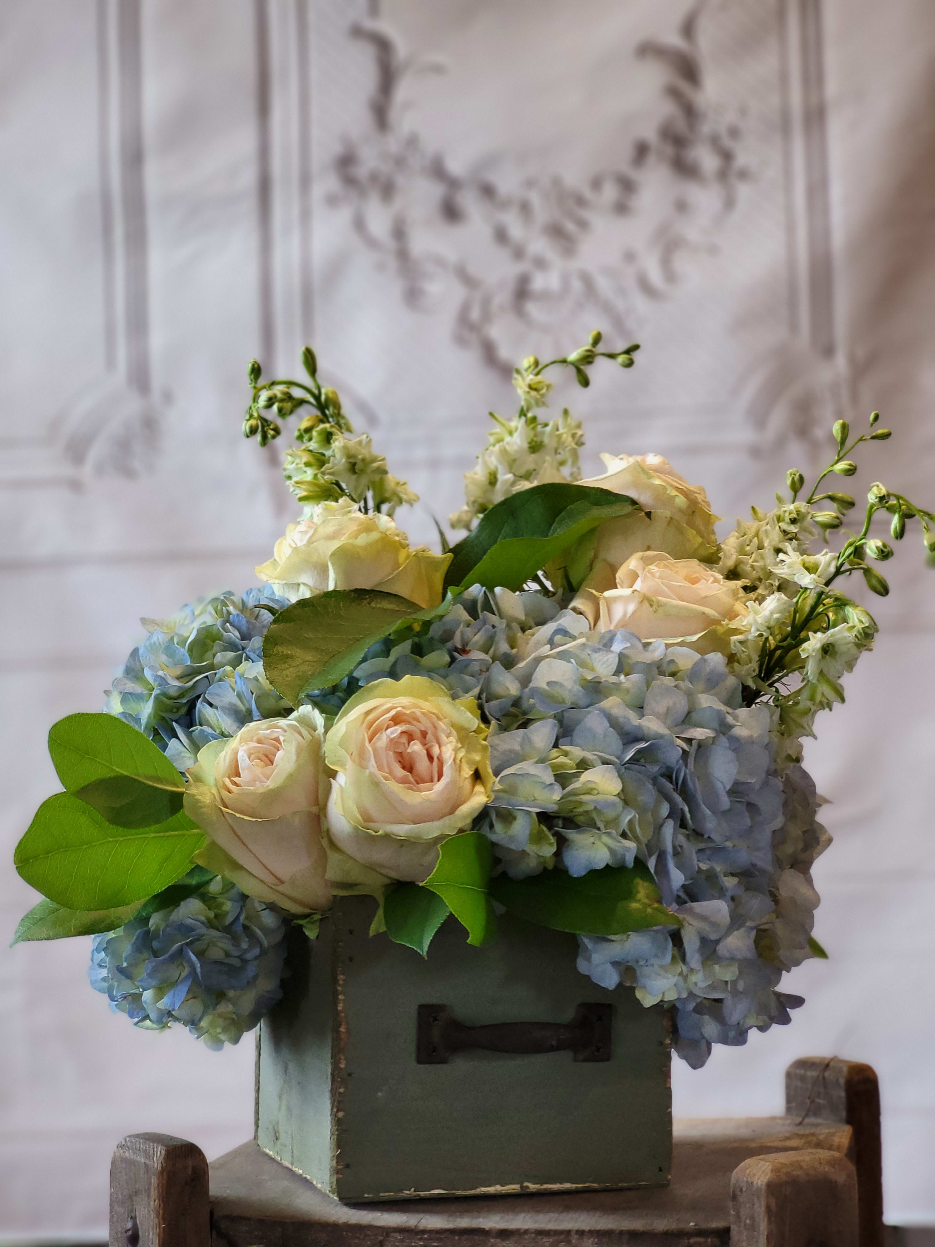 Blue hydrangeas and pale roses arranged in a green box
