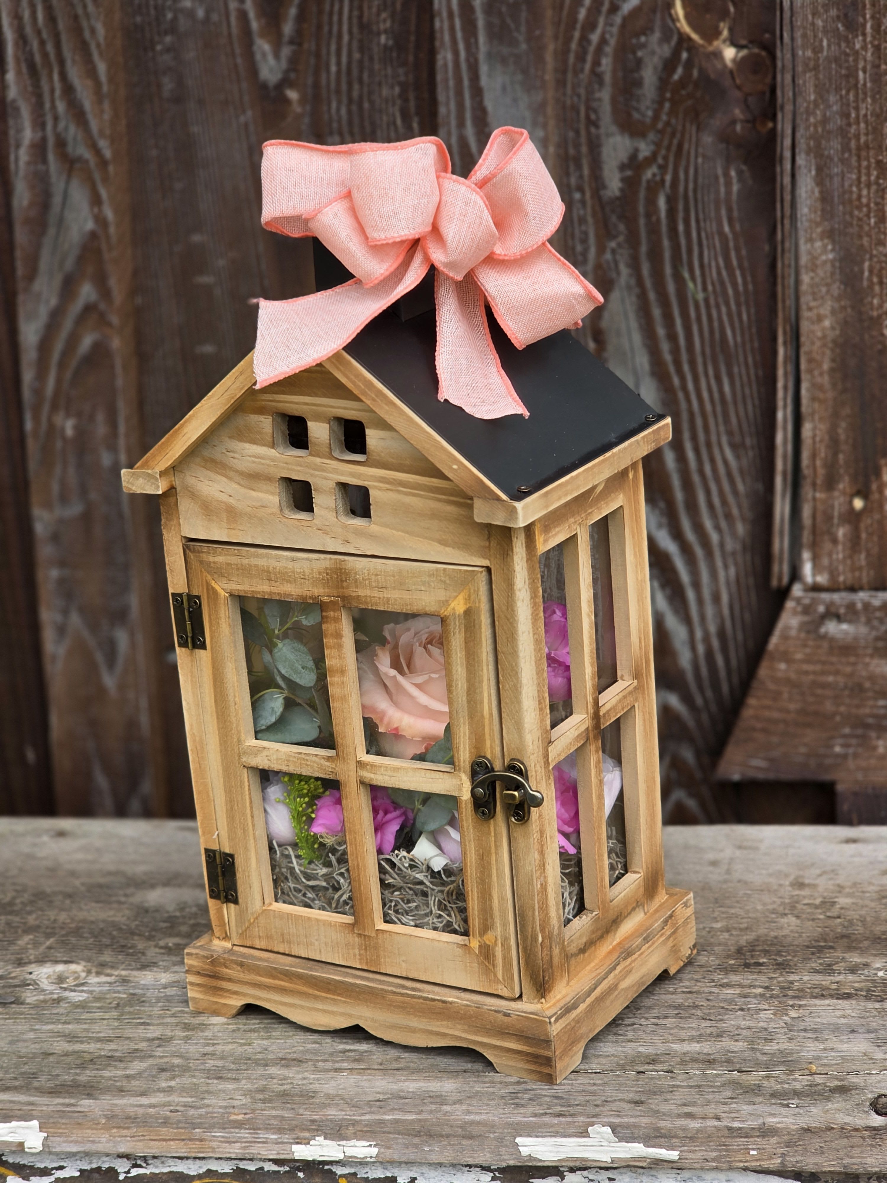 Wooden lantern with pink flowers inside and a pink bow on top